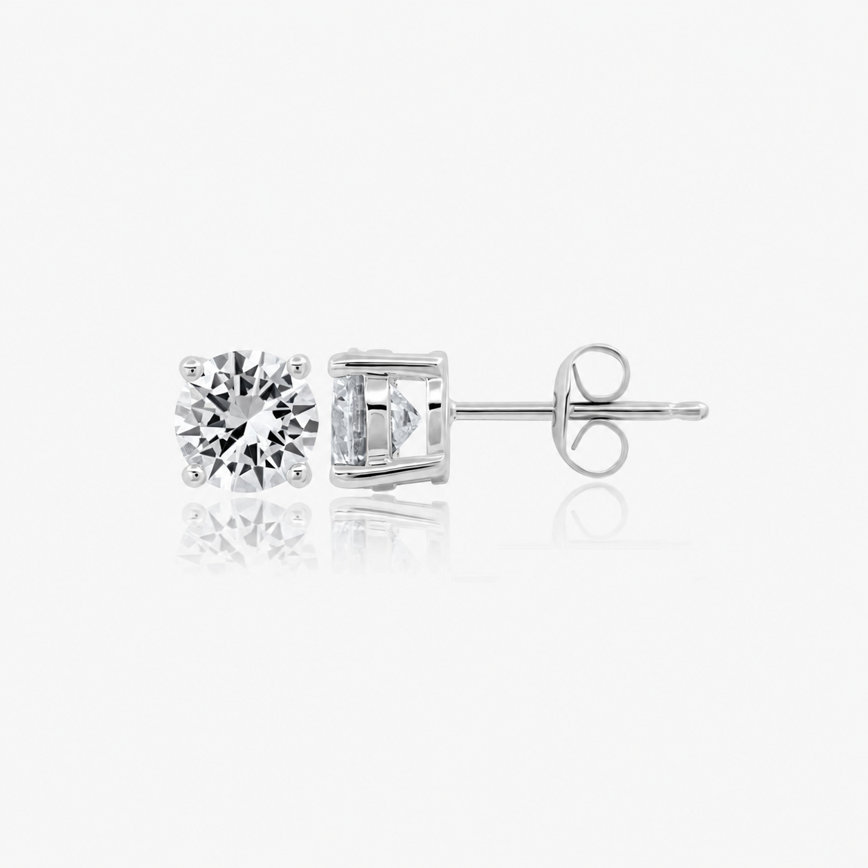 Pair of silver-toned stud earrings, each with a round, brilliant-cut clear stone in a 4-prong setting. One shows its post and