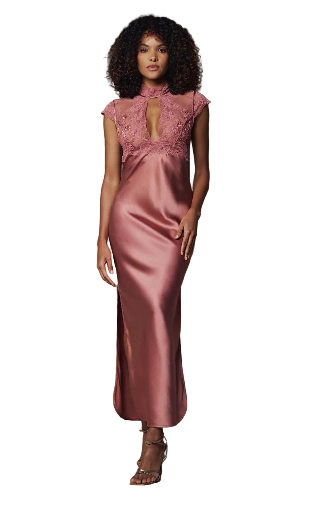A woman modeling a floor-length dusty rose satin gown with a lace high-neck bodice and cap sleeves, standing in front of a brown slatted wall.