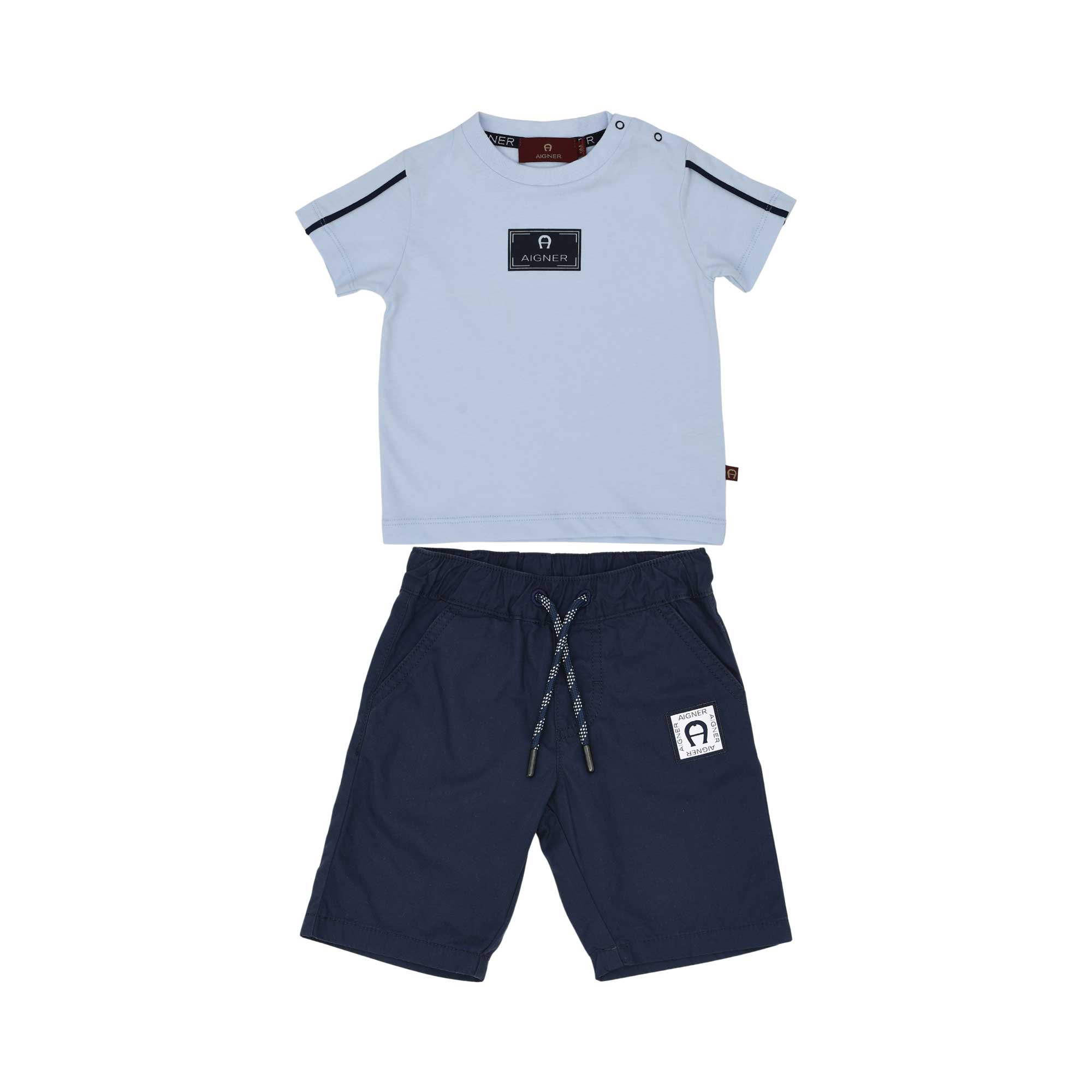 A two-piece baby boy's outfit by Aigner Kids featuring a light blue short-sleeved T-shirt with a navy logo patch and a pair of navy blue drawstring shorts with a matching logo on the leg.