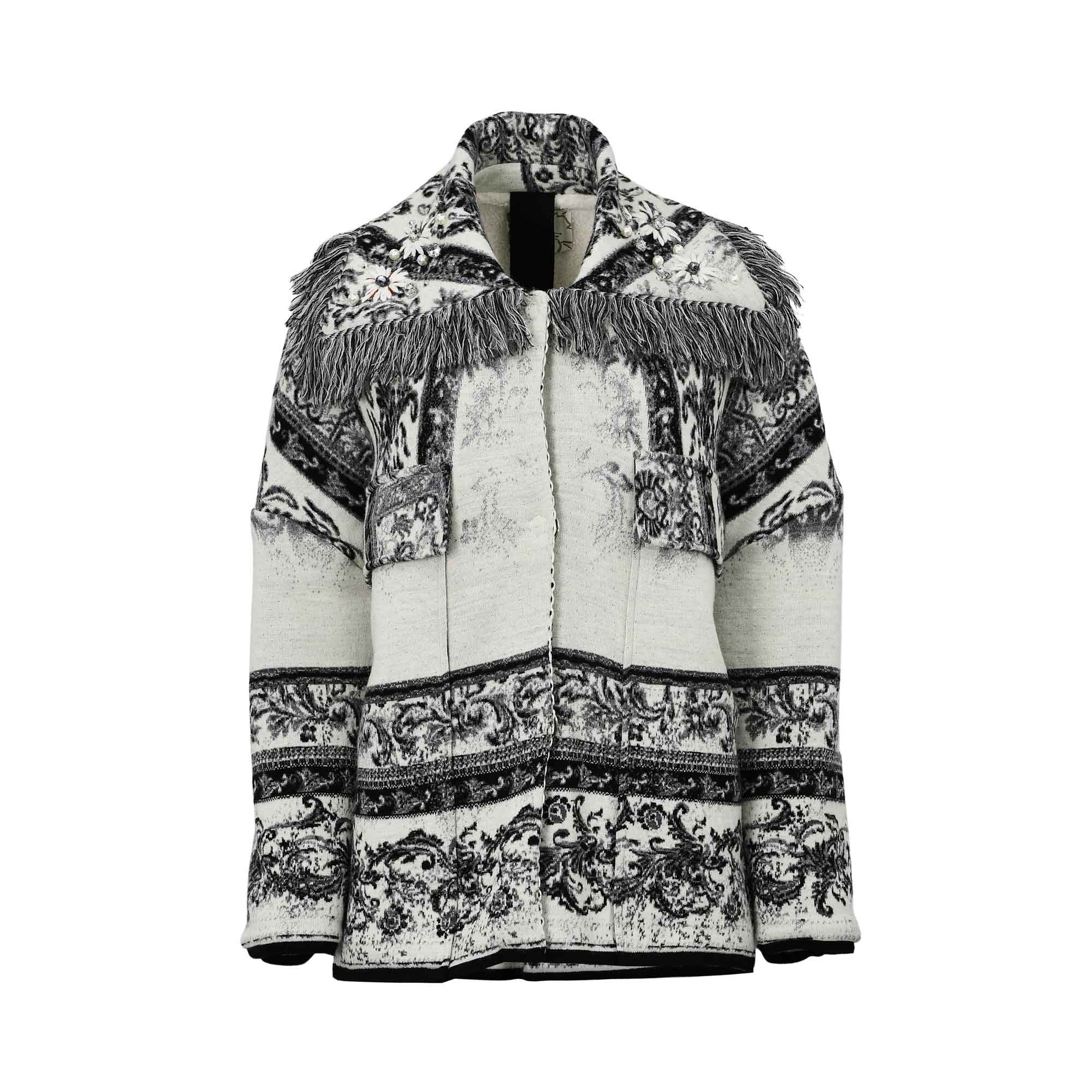 Front view of a cream and black tapestry knit jacket featuring intricate baroque patterns, a tiered charcoal fringe across the chest and shoulders, and decorative crystal floral appliqués on the lapels