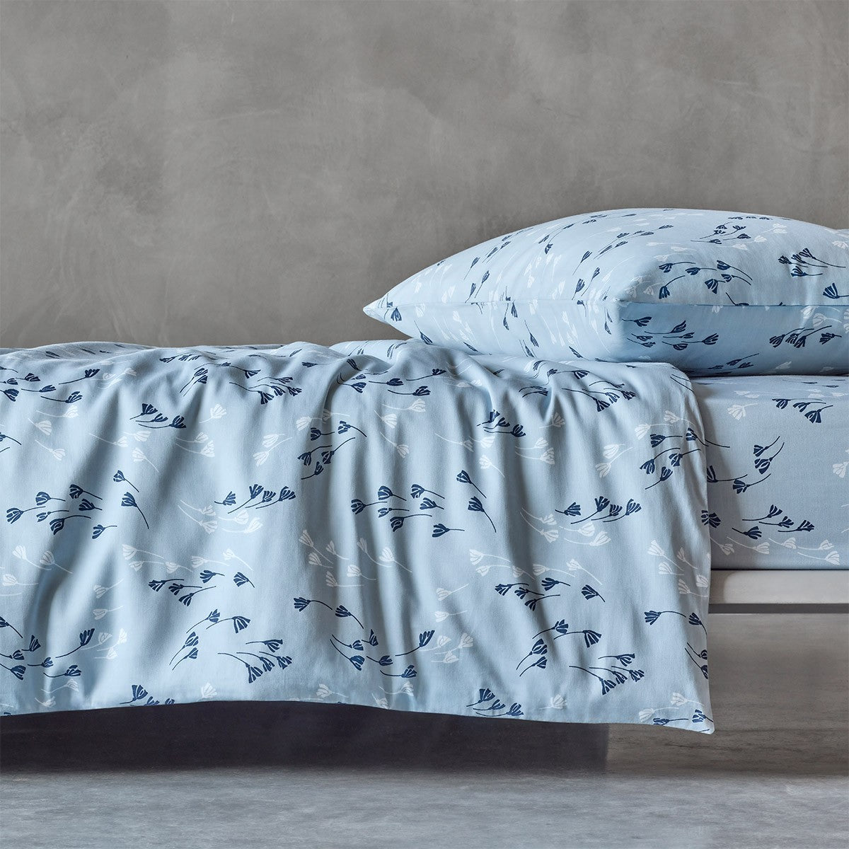 Light blue duvet cover and pillow case with a repeating pattern of dark blue and white stylised botanical sprigs.