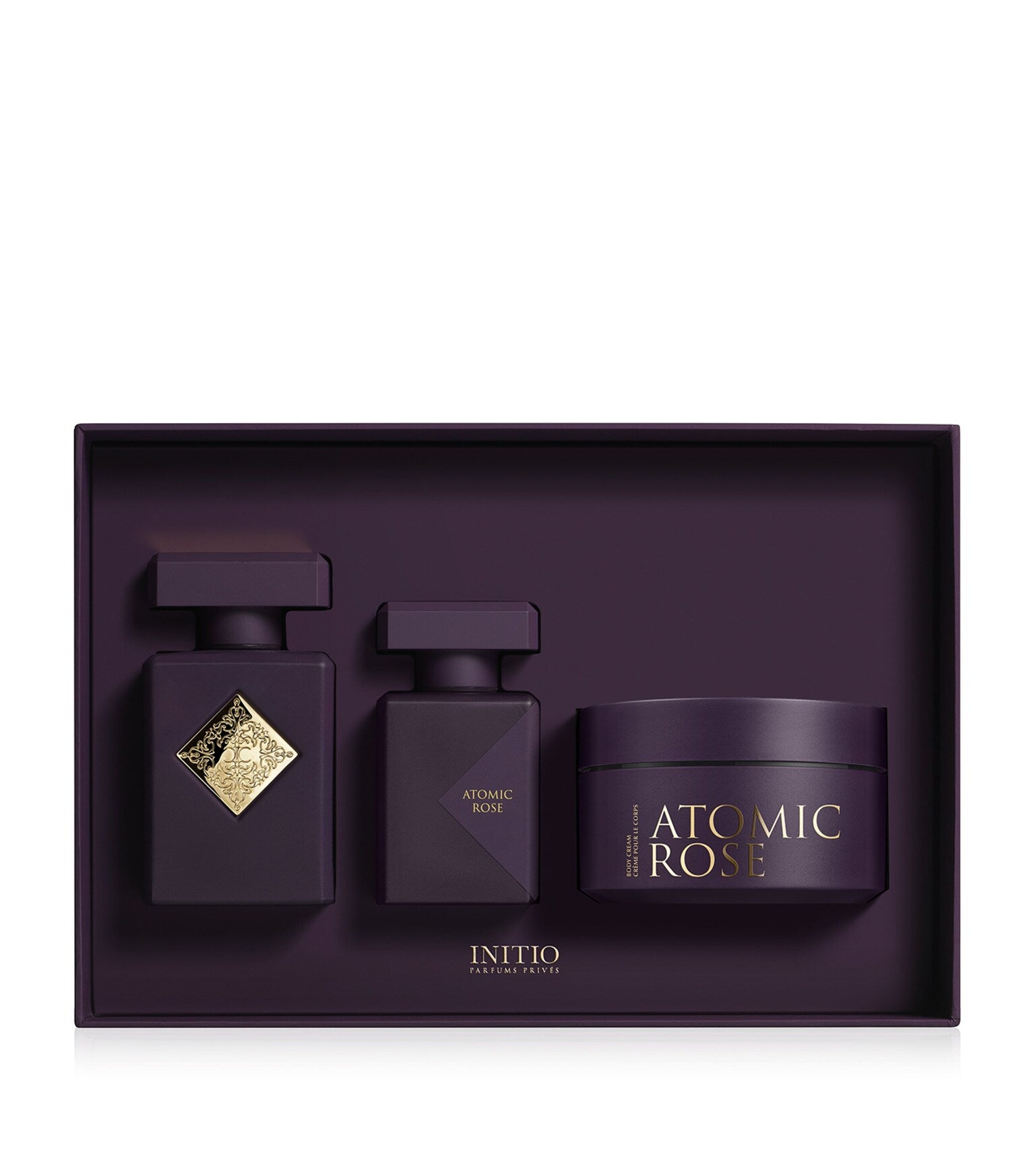 Initio Parfums Privés Atomic Rose luxury gift set resting inside a deep purple display insert, showcasing the gold-crested Eau de Parfum bottle, a matching hair perfume, and a scented body cream jar, available at blue salon.