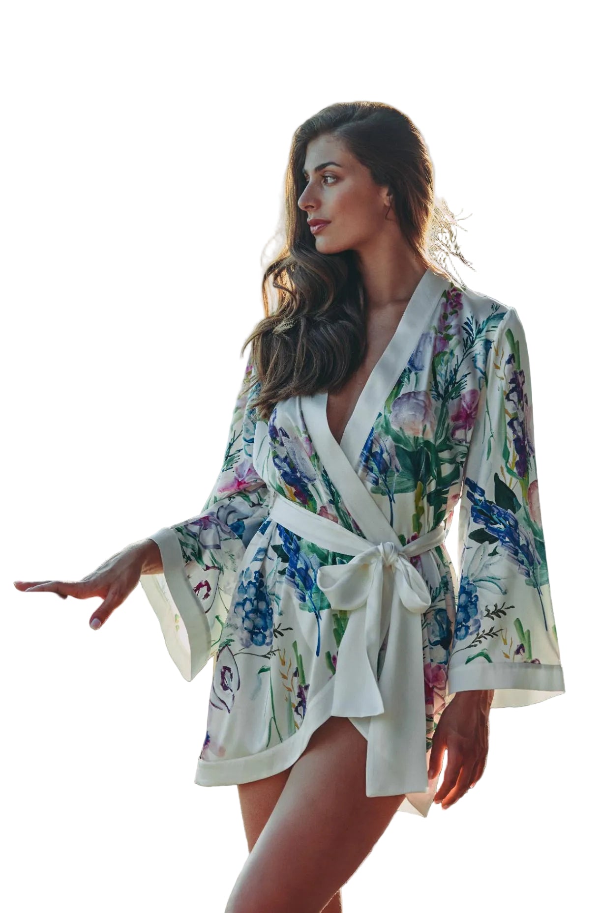 A woman wearing a white kimono-style robe with a colorful floral print and a tied waist sash, standing on a balcony with a railing and blurred outdoor scenery in the background.
