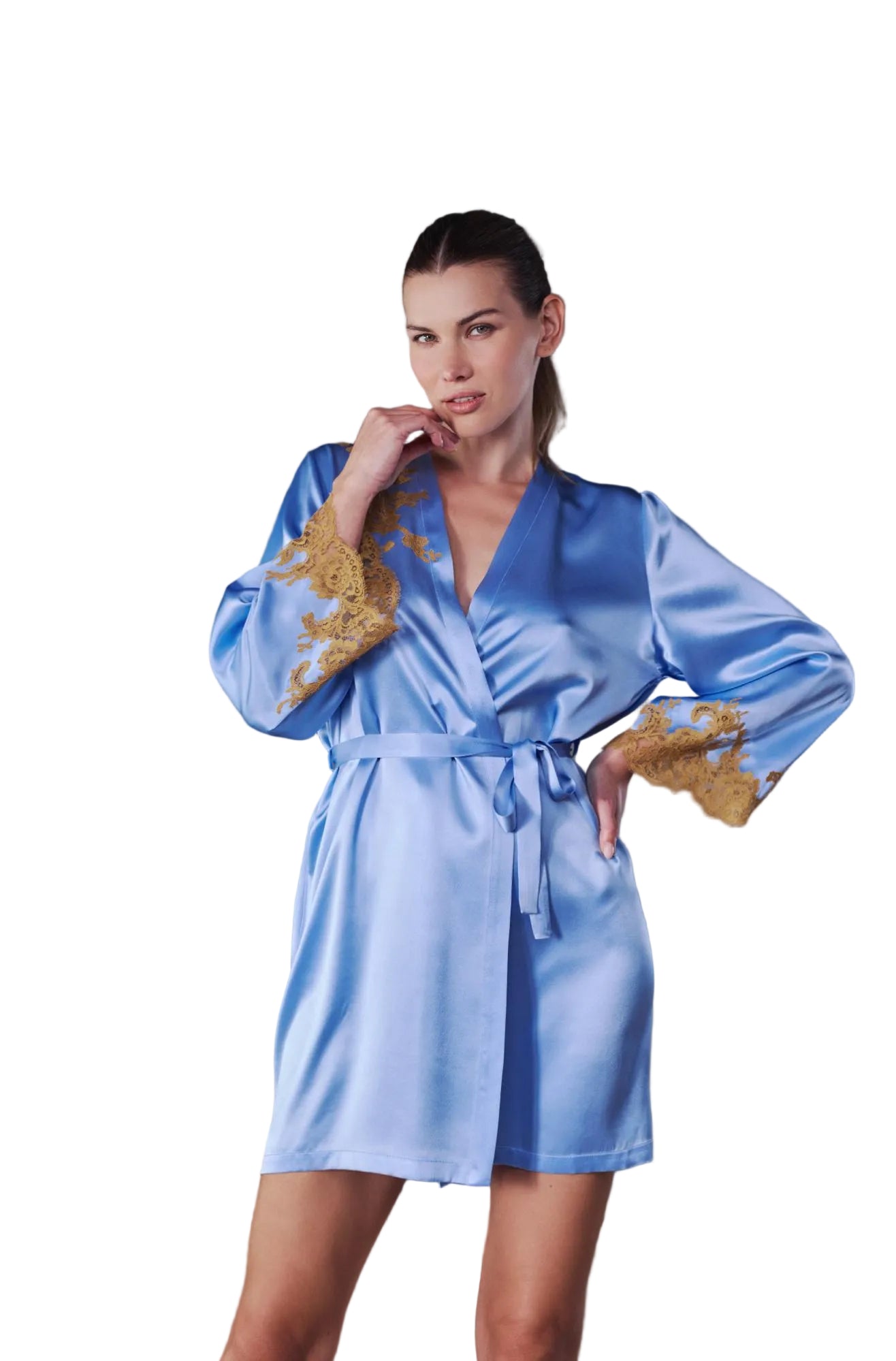 A woman modeling a light blue satin robe with gold embroidered details on the sleeves, standing in front of a gray wall and a light gray sofa.