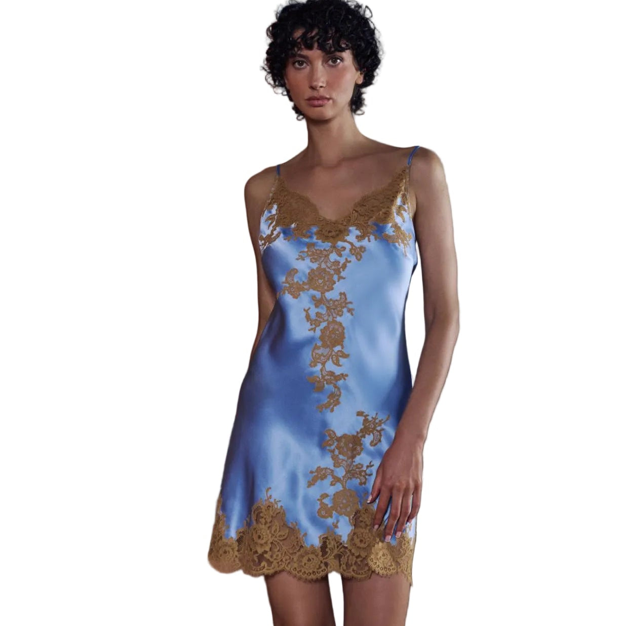 A woman wearing a light blue satin slip dress with gold floral embroidery and lace trim, standing in a doorway with a gray wall and terracotta-colored stairs behind her.