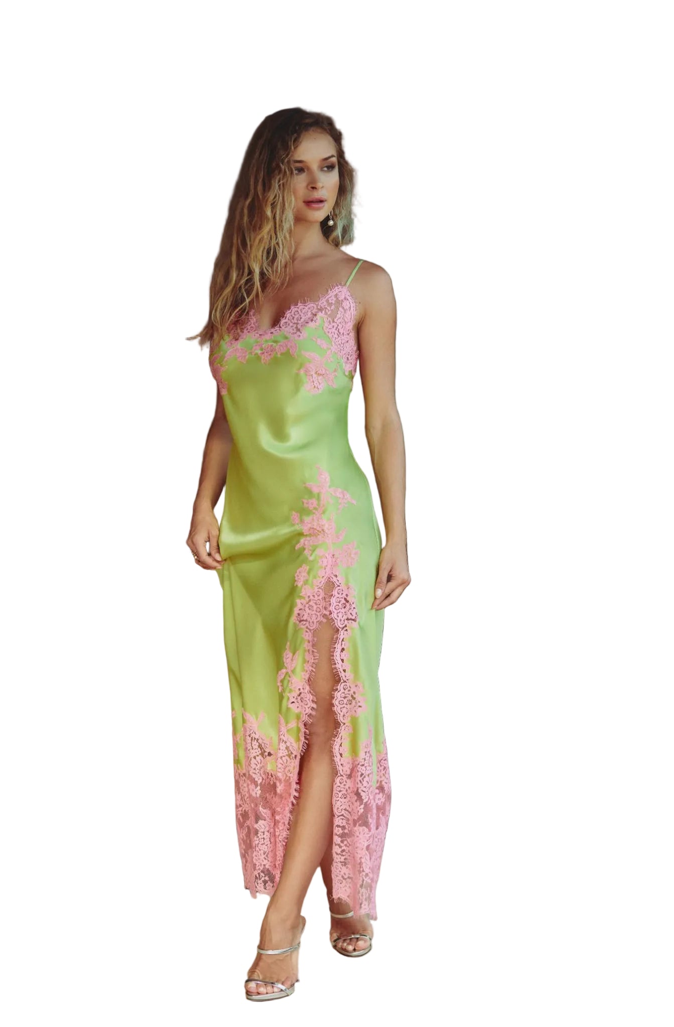 A woman models a lime green satin slip dress with pink floral lace trim and a high slit, standing in a modern home interior.