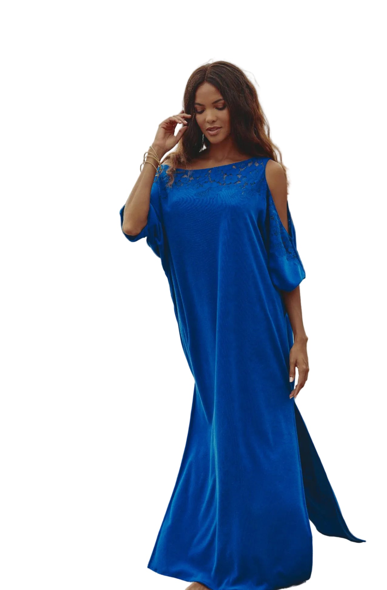 Woman in a blue dress standing on a beach with ocean and rocks in the background