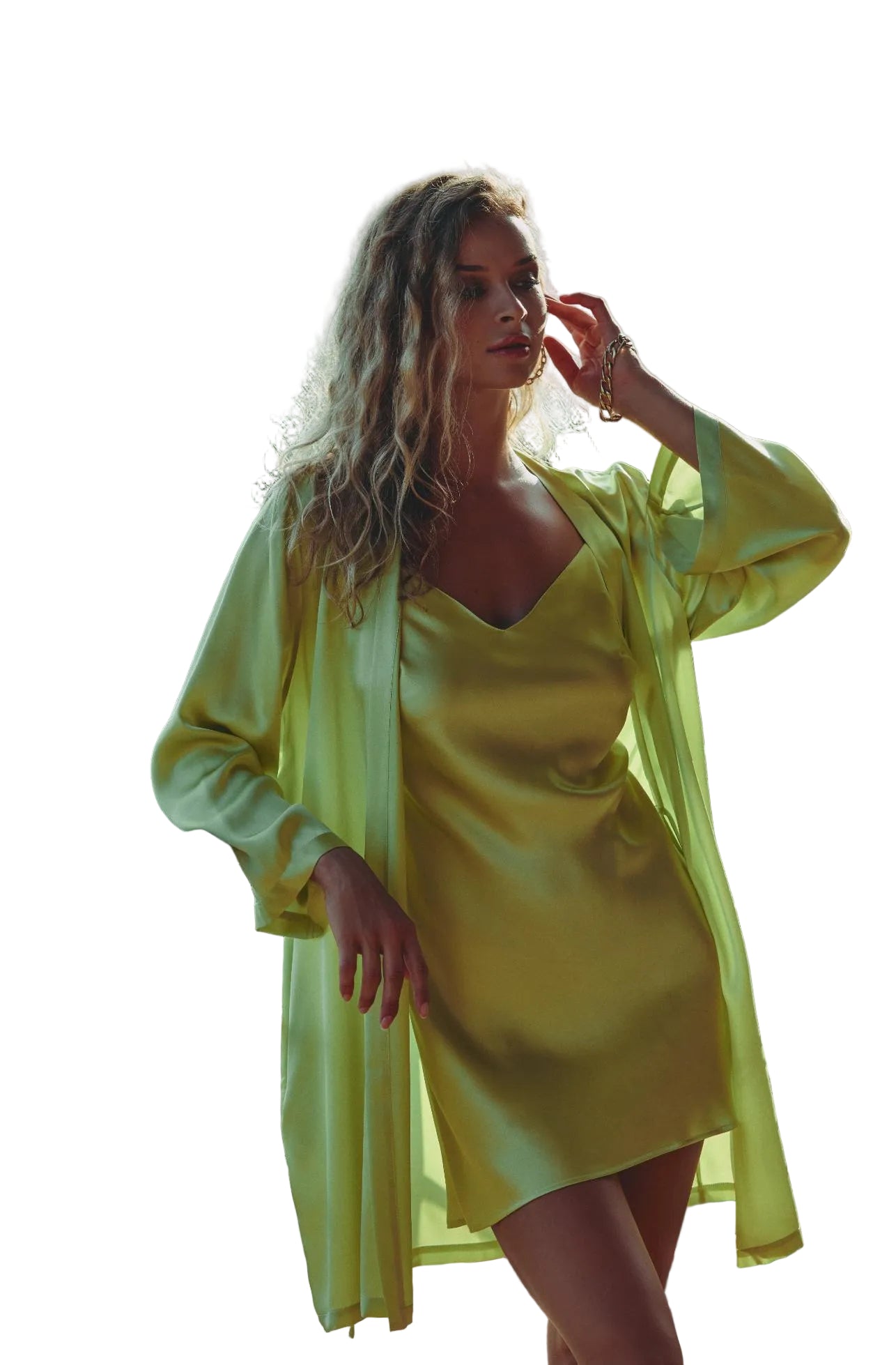 A woman wearing a bright yellow satin slip dress with a matching sheer long-sleeve robe, standing on a balcony with a blurred outdoor background.
