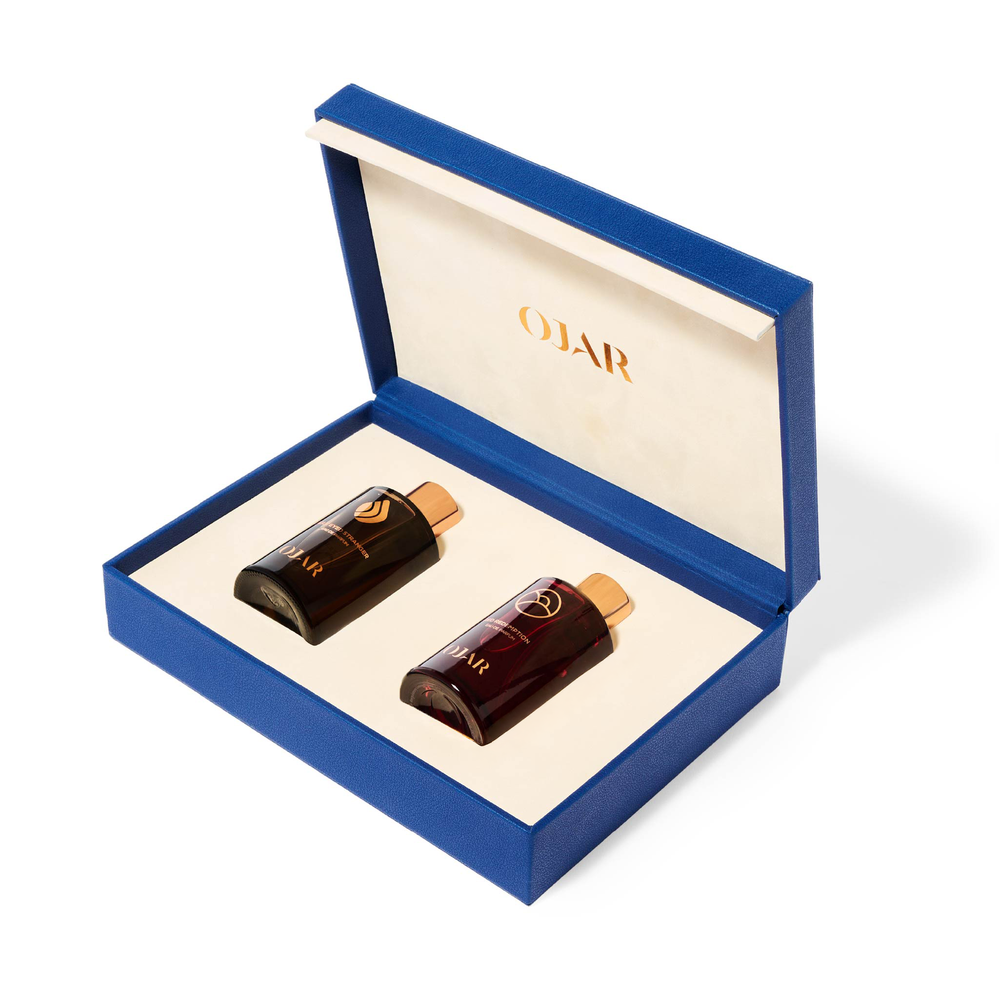 An open luxury gift box from OJAR titled "The Radiant Set." The box is a vibrant cobalt blue with a cream-colored interior holding two 15ml amber glass perfume bottles with copper caps. The internal lid features the OJAR logo in gold.