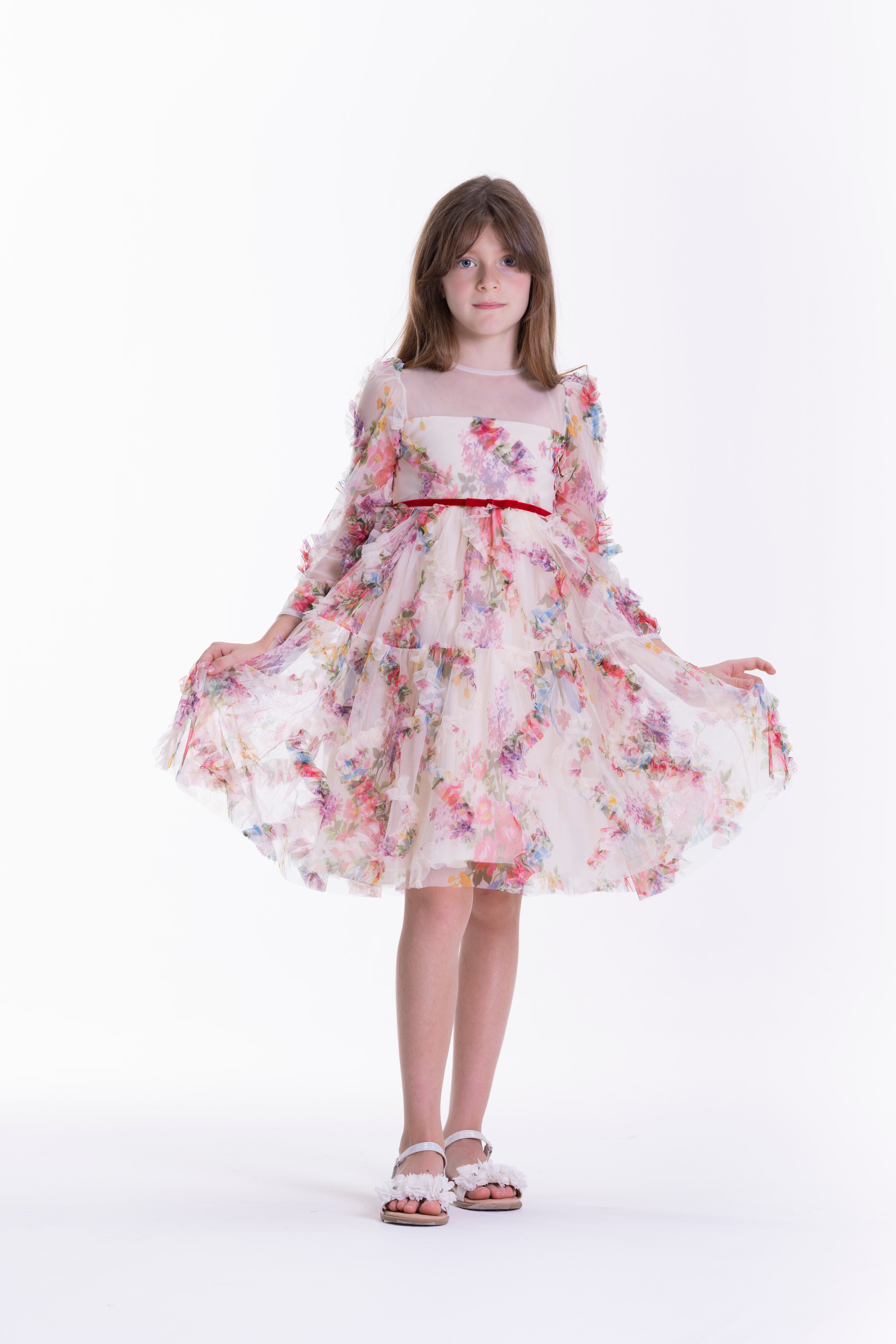 Beige kids' dress with a multi-coloured floral pattern, sheer round neckline, long ruffled sleeves, and a red velvet waist ri