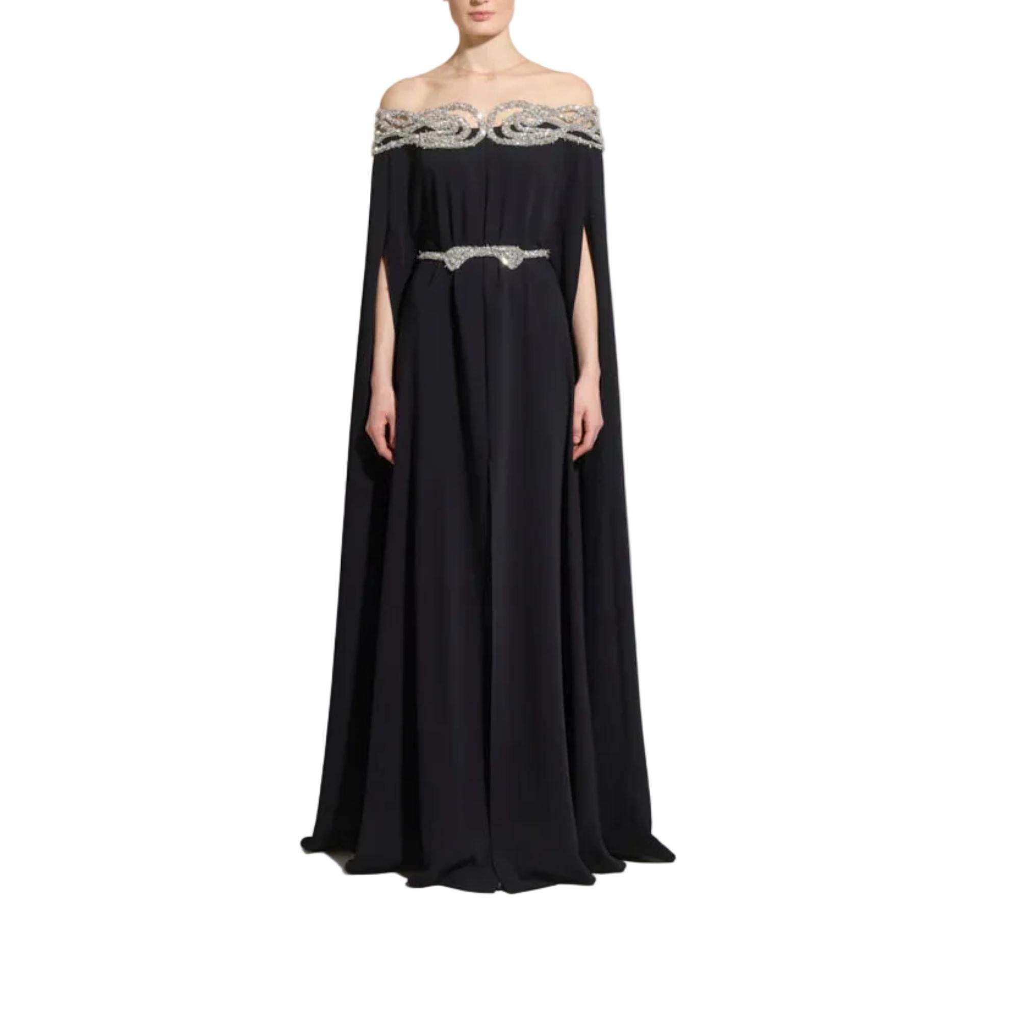 A floor-length off-the-shoulder black gown with a draped cape-like silhouette, ornate silver beaded detailing across the neckline and waist, and a flared skirt, shown on a model against a plain white background.