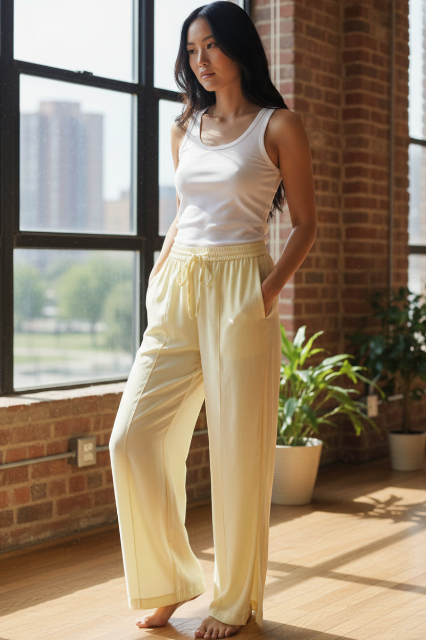 Pale yellow wide-leg trousers with an elasticated drawstring waist, side pockets, vertical front seams, and small hem slits.