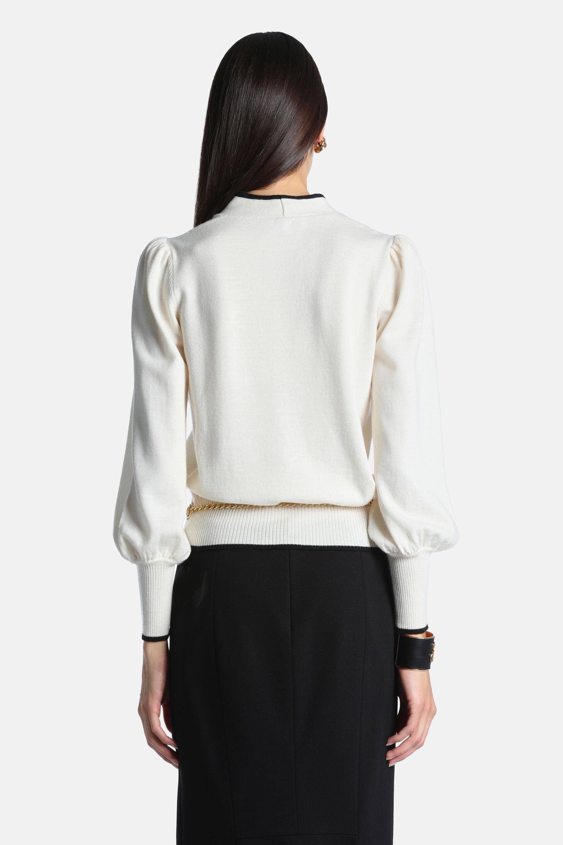 Cream knit pullover with puffed balloon sleeves, ribbed cuffs and hem, and black trim on the high neck and cuffs. A gold-tone