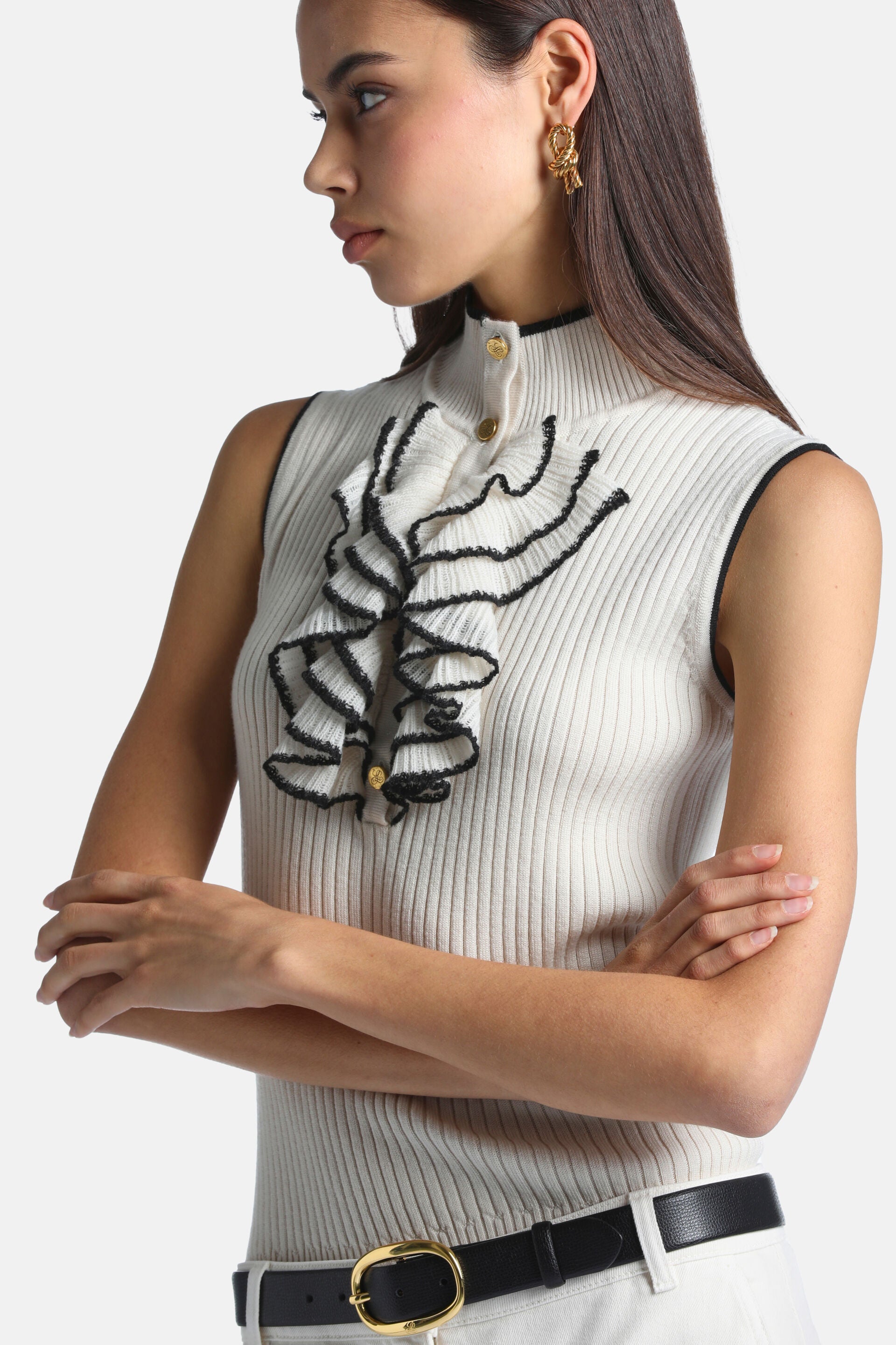 Cream ribbed knit sleeveless pullover with black trim on mock neck and armholes. Front has black-edged ruffles and gold-toned