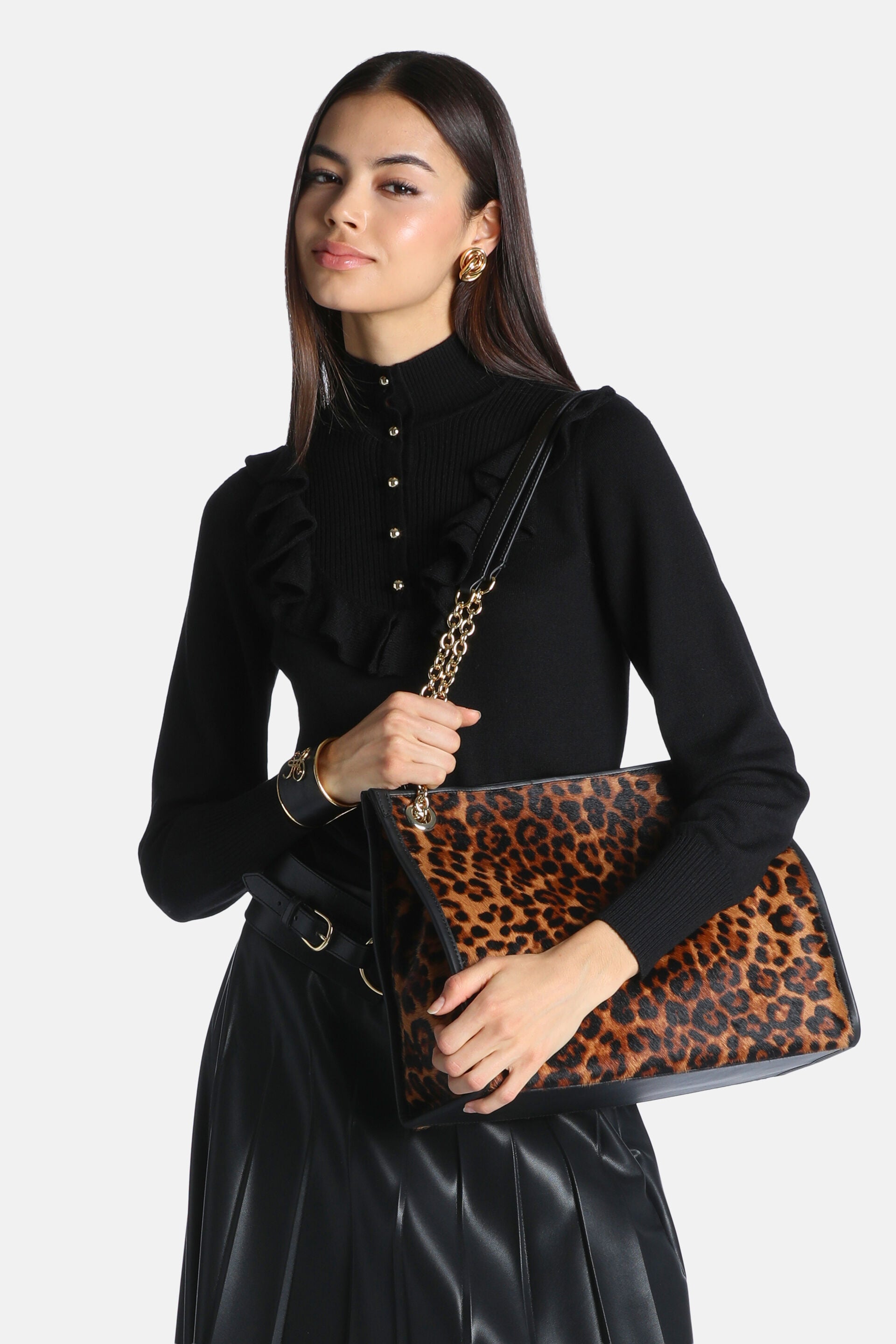 Black long-sleeved pullover with a high neck, ribbed center panel, gold-toned buttons, and ruffled trim across the chest. Rib