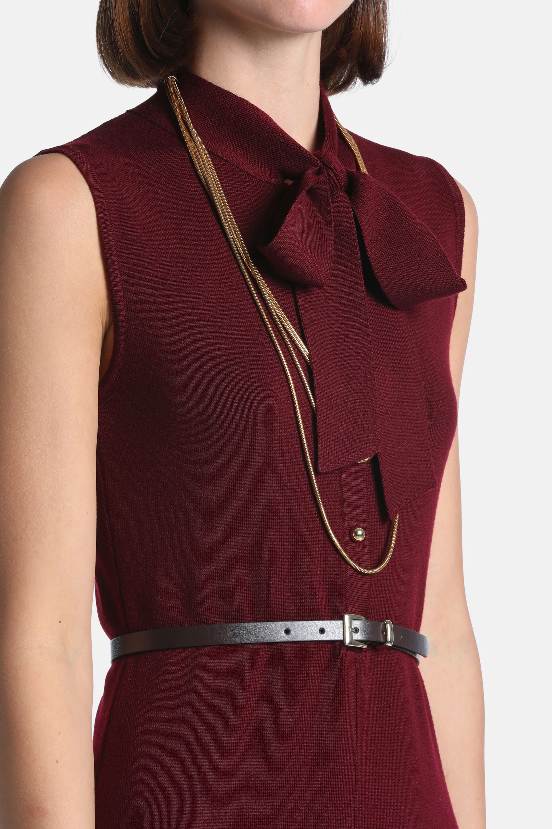 Sleeveless burgundy knit dress with a collared pussy-bow tie. Features a gold-toned stud and a thin dark brown belt with a si