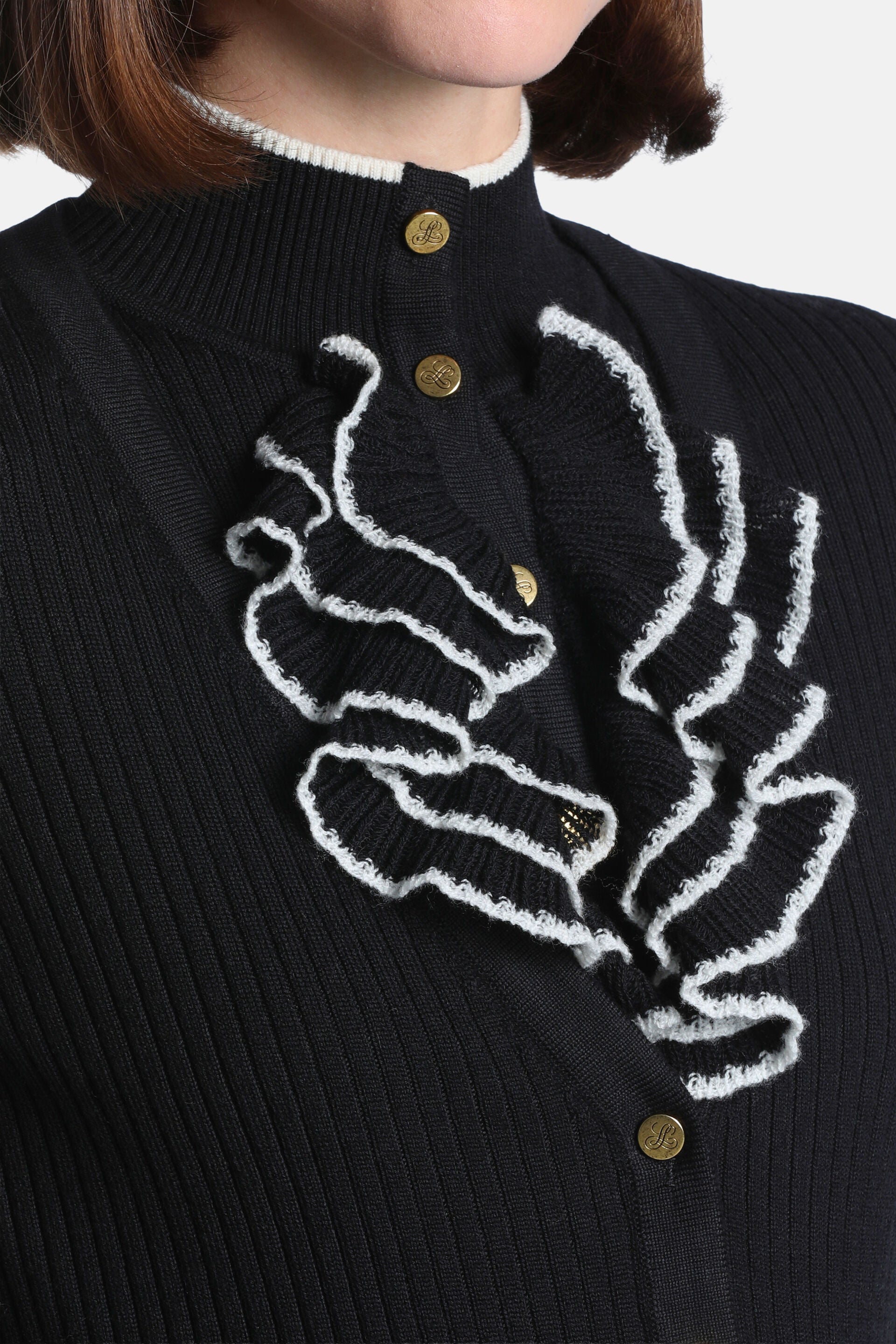 Black ribbed knit jacket with white-trimmed stand collar, gold-toned 'L' buttons, and ruffled placket with white edges.