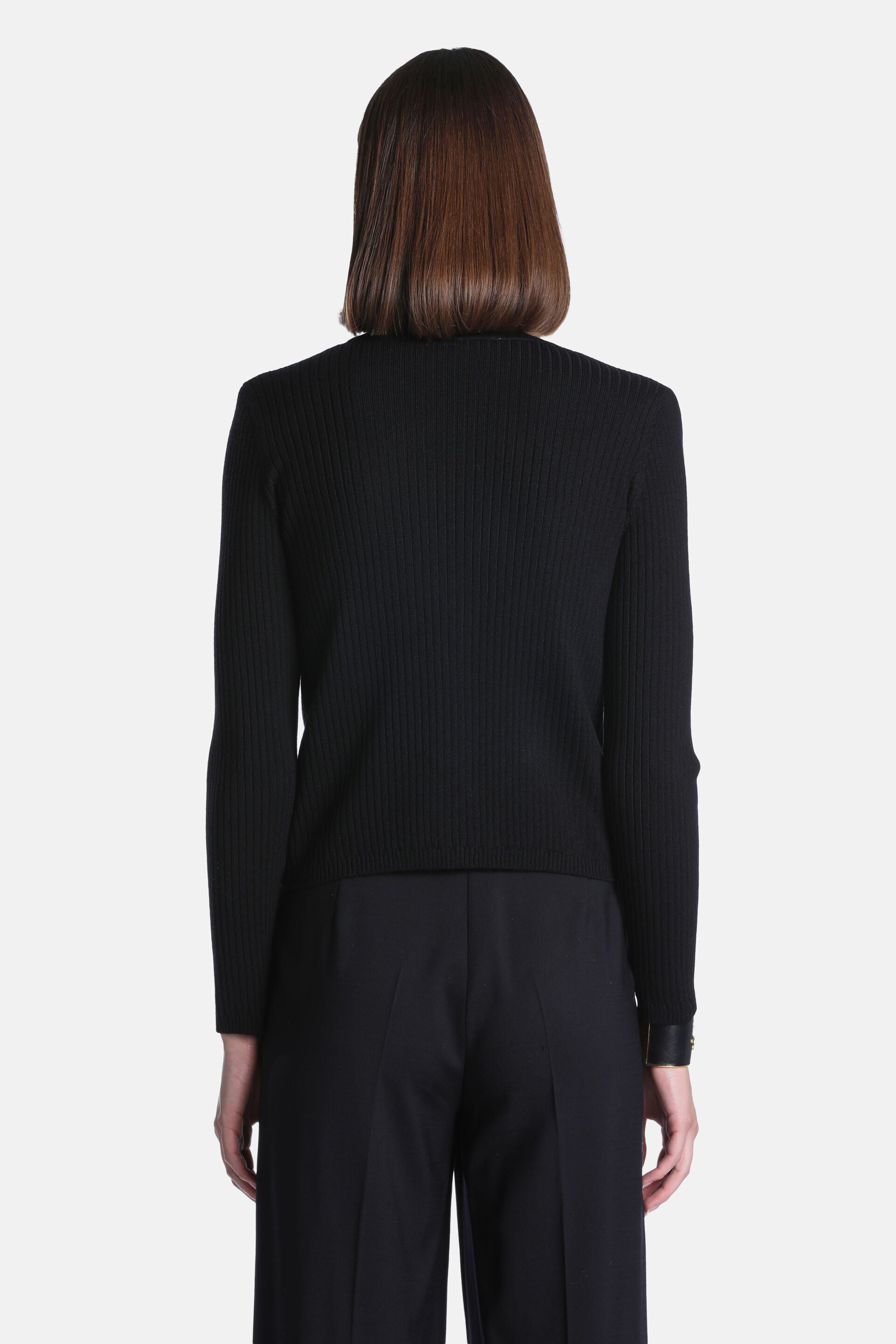Black ribbed knit jacket with long sleeves and a straight hem. The left cuff features a black band with a small gold-toned de