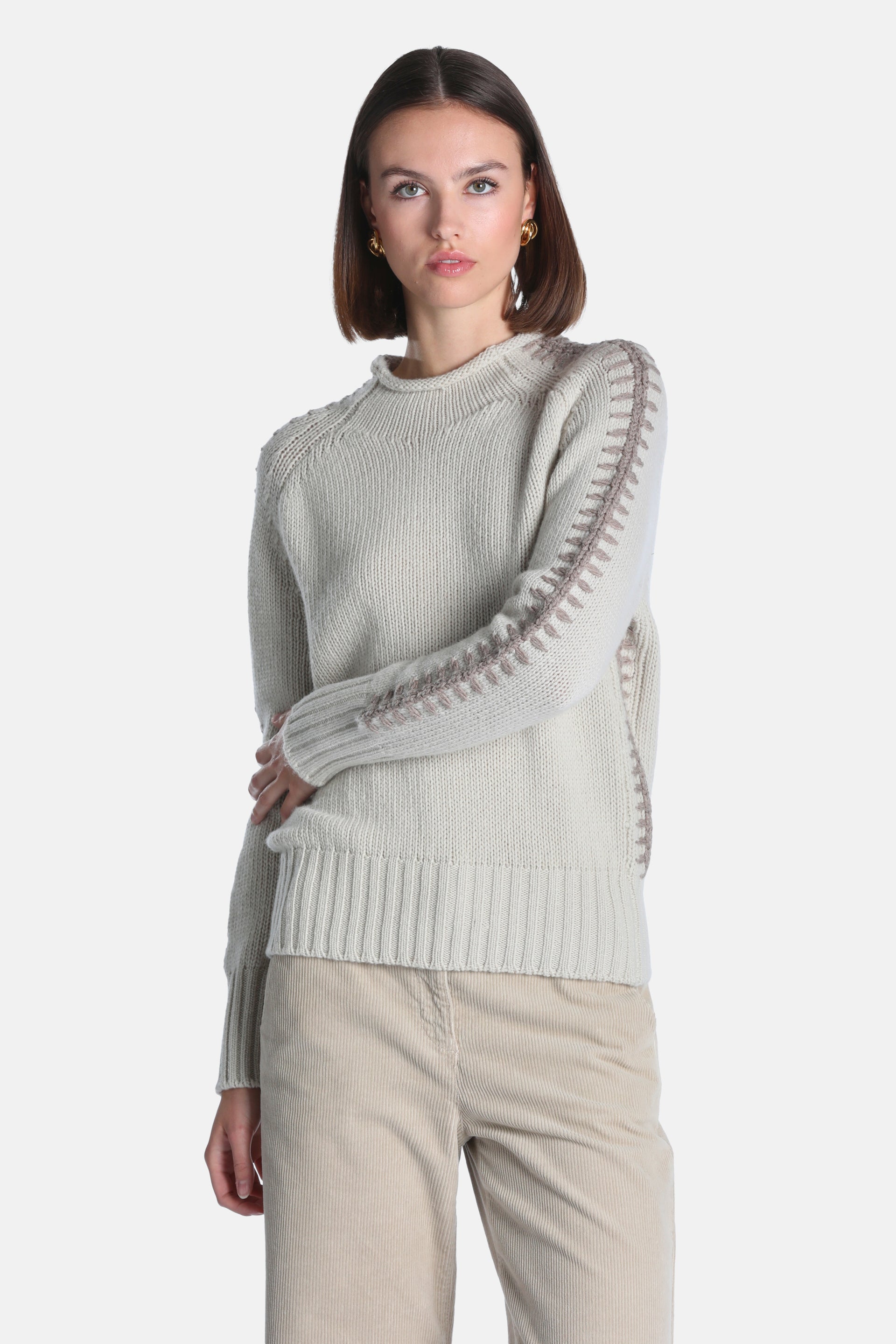 Beige knit pullover sweater with long raglan sleeves, ribbed trims, and brown decorative stitching along seams.