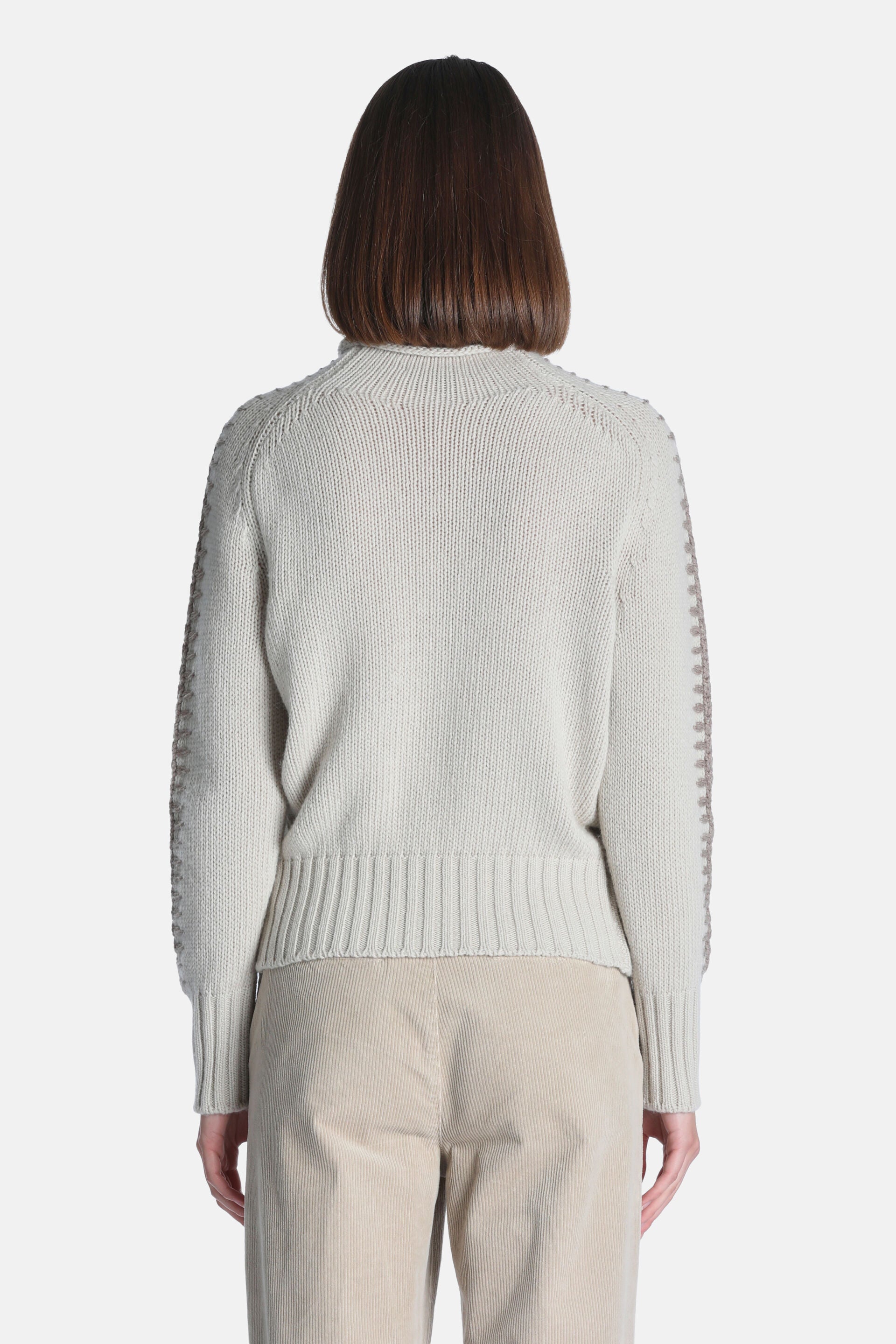 Beige knit pullover with a ribbed mock neck, cuffs, and hem. Features decorative brownish-beige stitching along the raglan sl