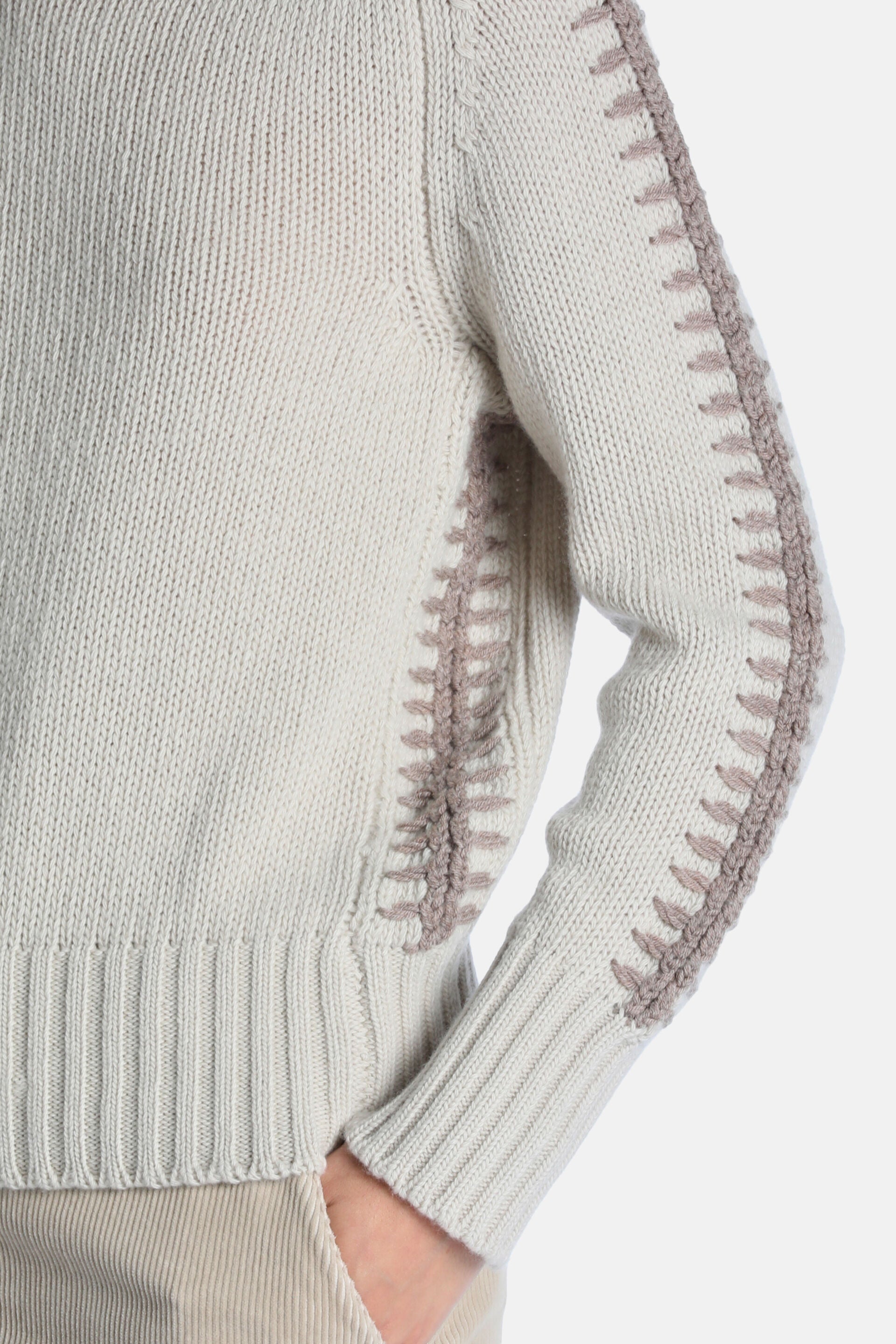 Beige knit pullover with ribbed cuffs and hem. Darker beige decorative ladder stitching on the outer sleeve and side.