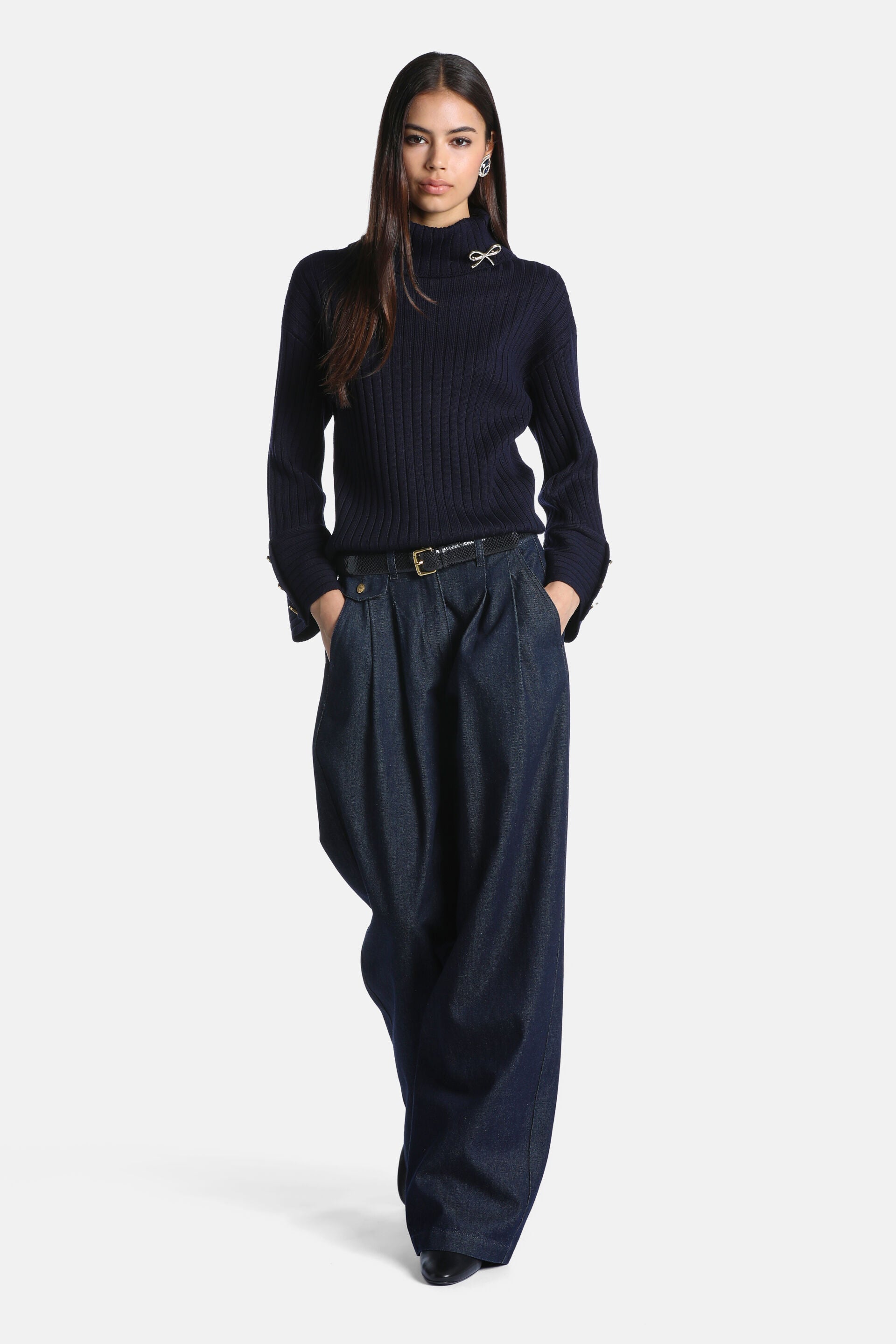 Navy blue ribbed knit turtleneck pullover with long sleeves, folded cuffs with gold-toned buttons, and a silver-toned bow bro