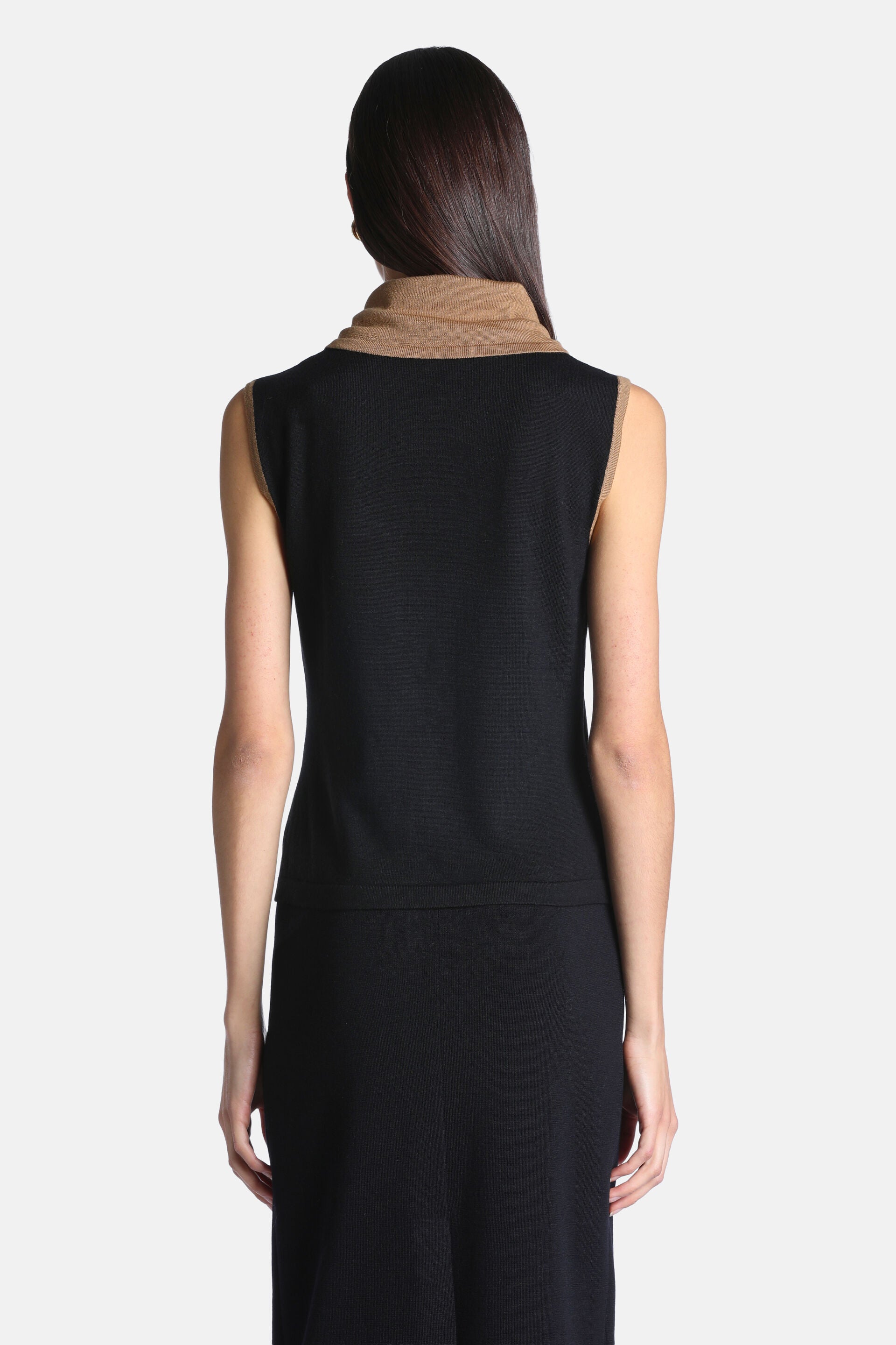 Black sleeveless sweater with a camel cowl neck and camel trim on the armholes, seen from the back.