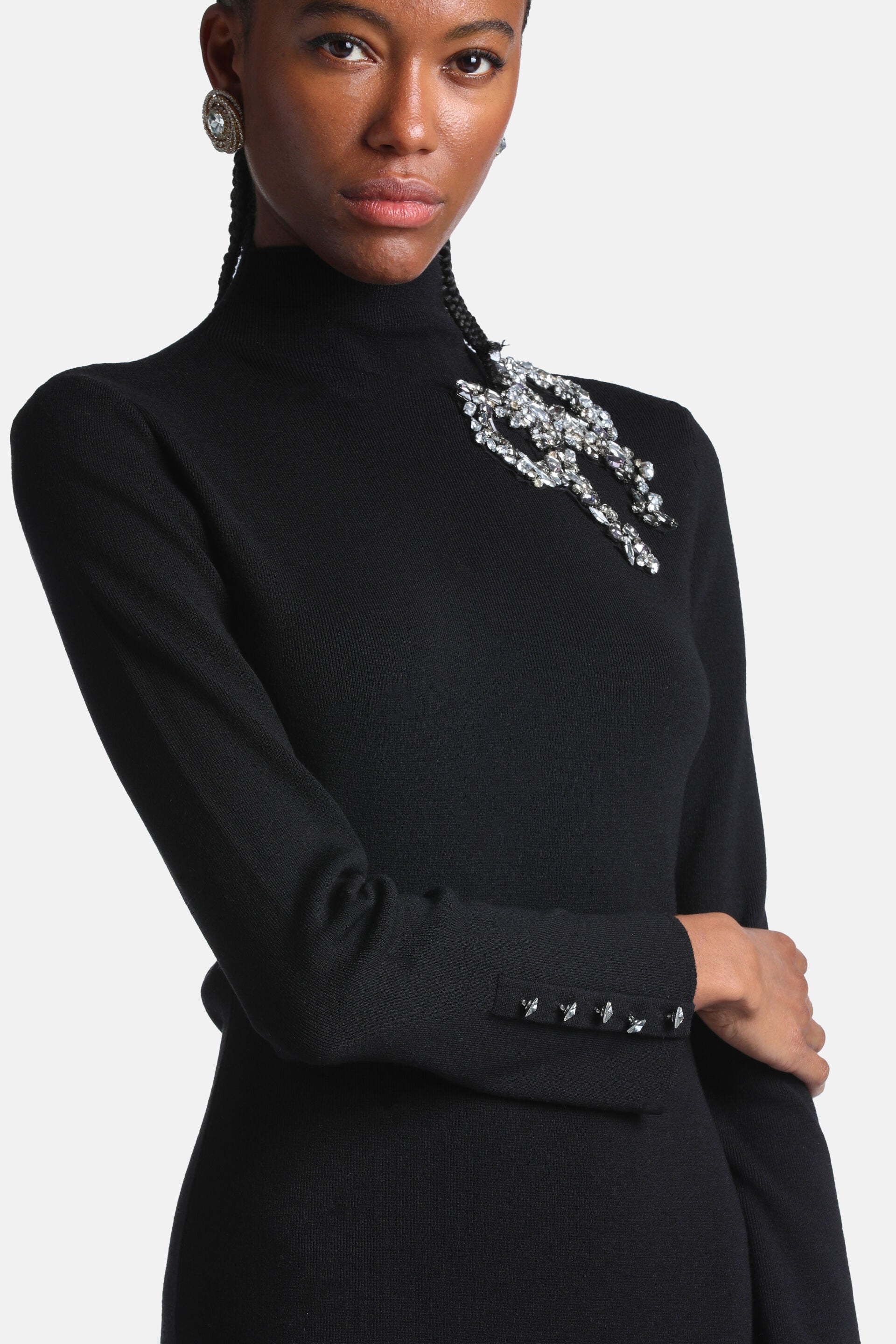 Black knit turtleneck dress with long sleeves. Features a sparkling crystal embellishment on the left shoulder and four small