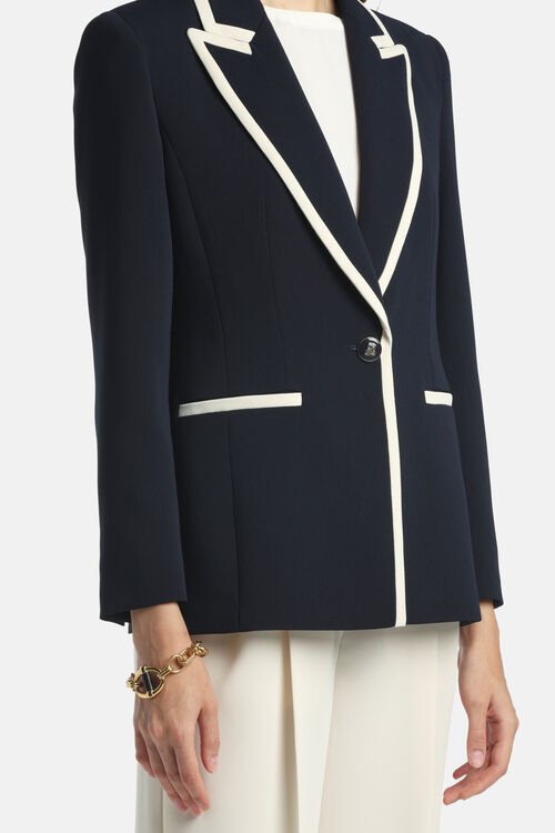 Navy blue blazer with off-white trim on notched lapels, front opening, and two horizontal welt pockets. Single dark button cl