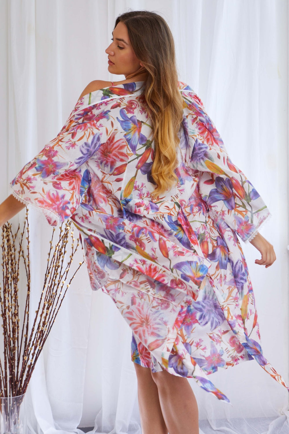 White voile kimono wrapover with vibrant multi-colored floral print, wide sleeves with white lace trim, and a matching self-t