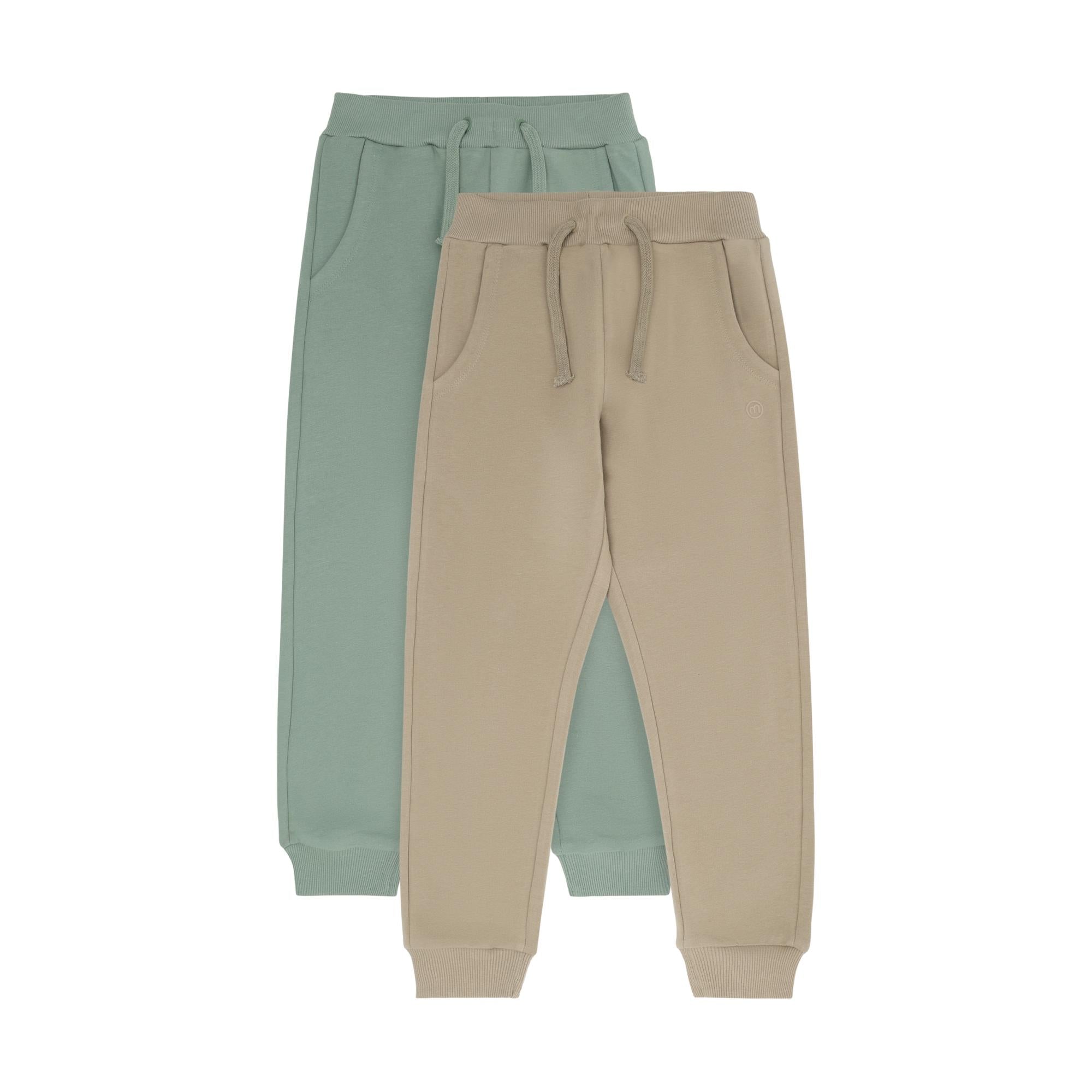 Two pairs of kids' sweatpants, one light sage green and one light beige, with elasticated drawstrings and ribbed cuffs.
