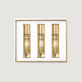 Three clear glass perfume bottles with gold-toned caps and labels, containing light amber liquid, presented in a white box wi