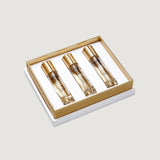 White and gold-toned gift box holding three clear glass perfume bottles, each with a gold-toned cap and amber liquid.