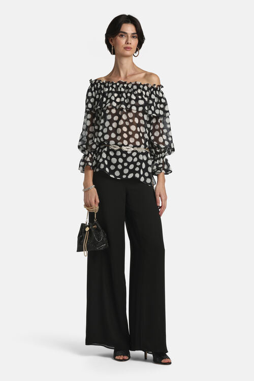 Black sheer off-shoulder blouse with white polka dots, ruffled neckline, voluminous sleeves with ruffled cuffs, and an asymme