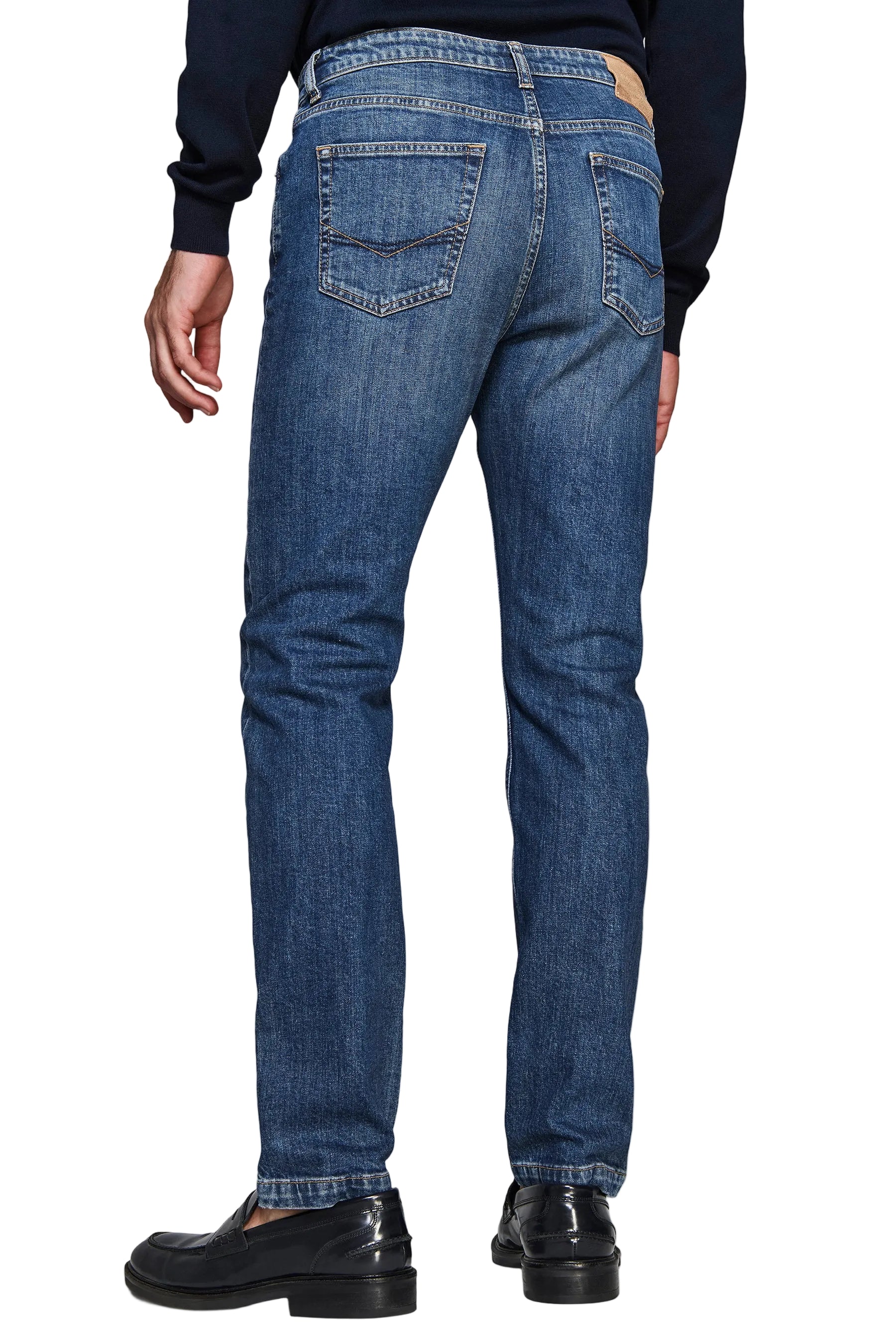 Medium blue denim jeans with a straight leg fit, featuring two back pockets with V-shaped stitching and a light brown patch o
