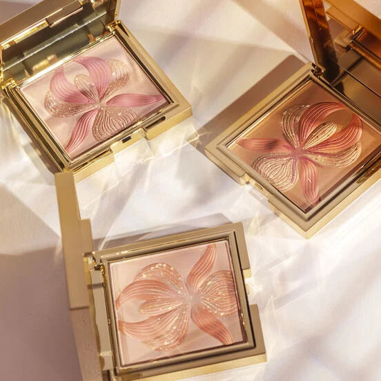 Gold-toned square compact with shimmery pink pressed powder featuring an embossed rose orchid design with textured, gold-tone