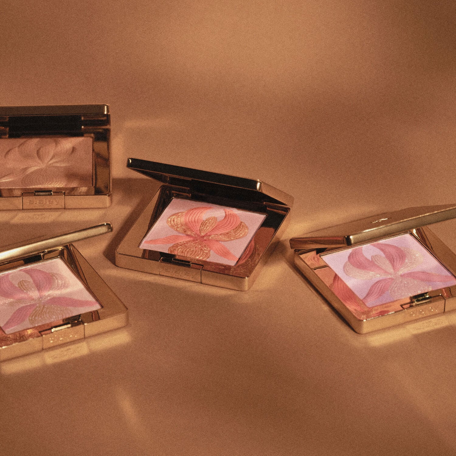 Gold-toned square compact with an open lid revealing a pressed powder with a raised coral and gold-toned orchid design.