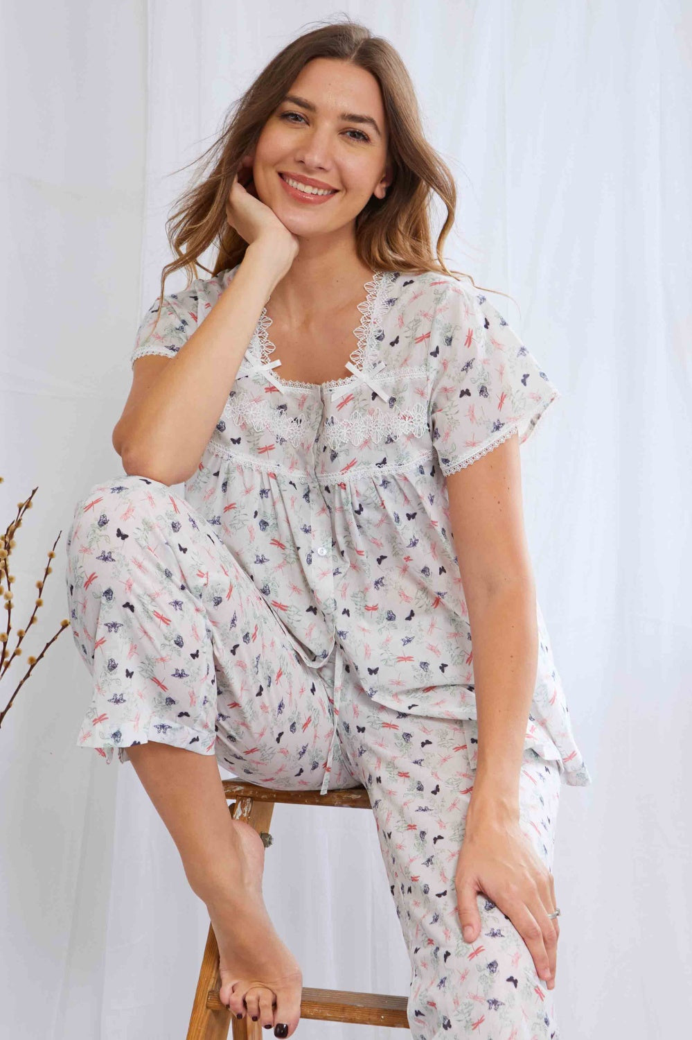 Pajama set with butterfly and flora print. Button-up top has lace trim, bows, cap sleeves. Drawstring pants with ruffled cuff
