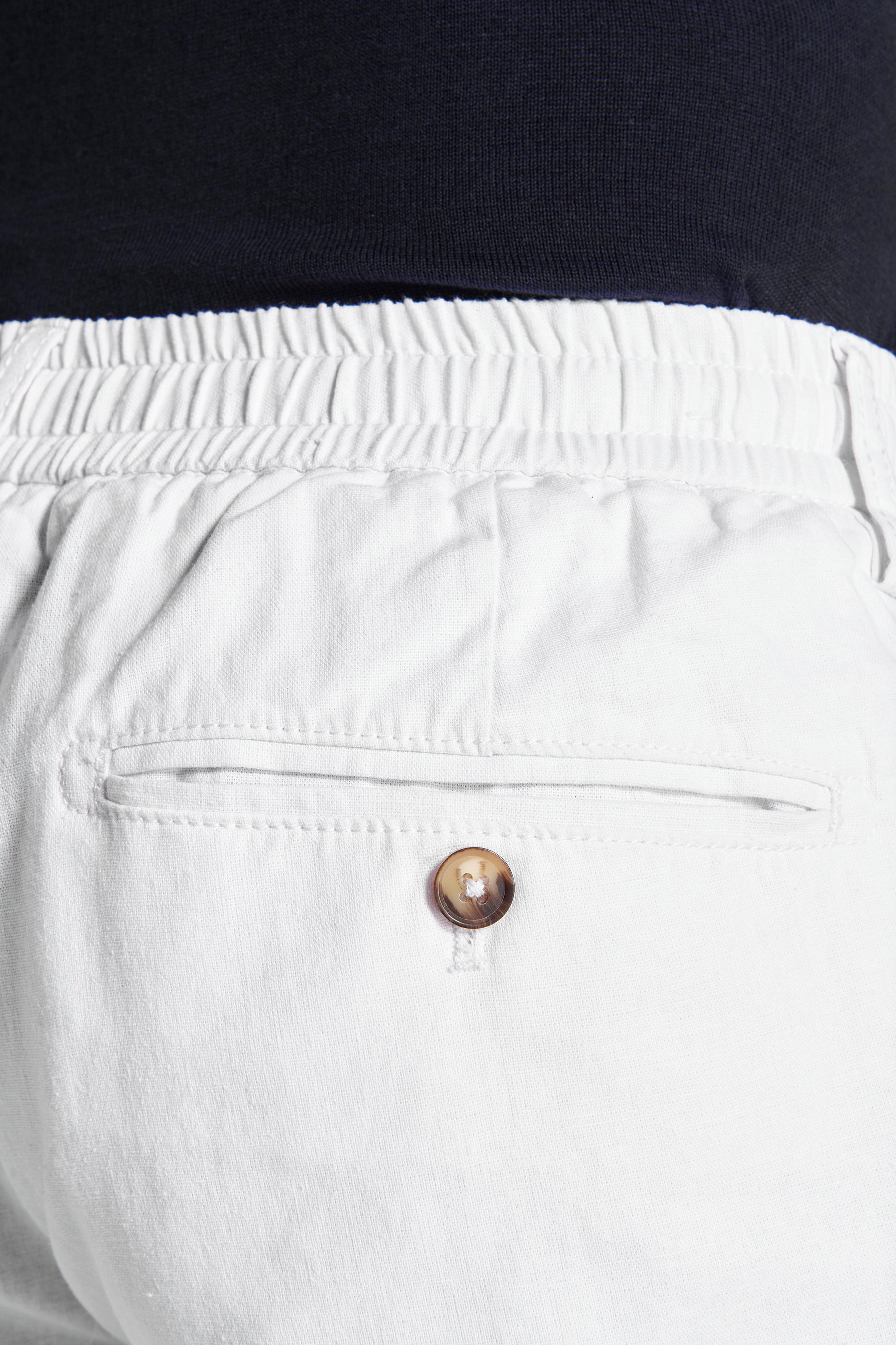 White trousers with an elasticated waistband and a single back welt pocket with a brown mottled button.