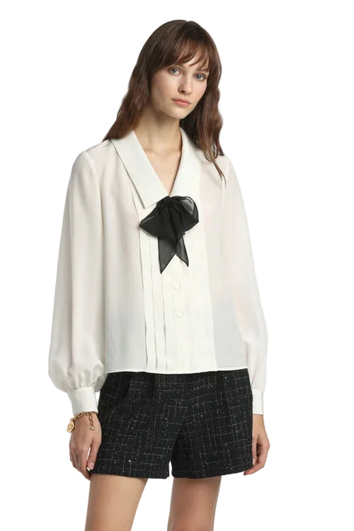 Off-white Crêpe de Chine shirt with a pointed collar, button front, vertical pleats, and a black sheer bow. Long gathered-cuf
