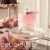 Clear glass perfume bottle with light pink liquid, gold-toned sprayer, and a glittery pink sheer fabric bow.