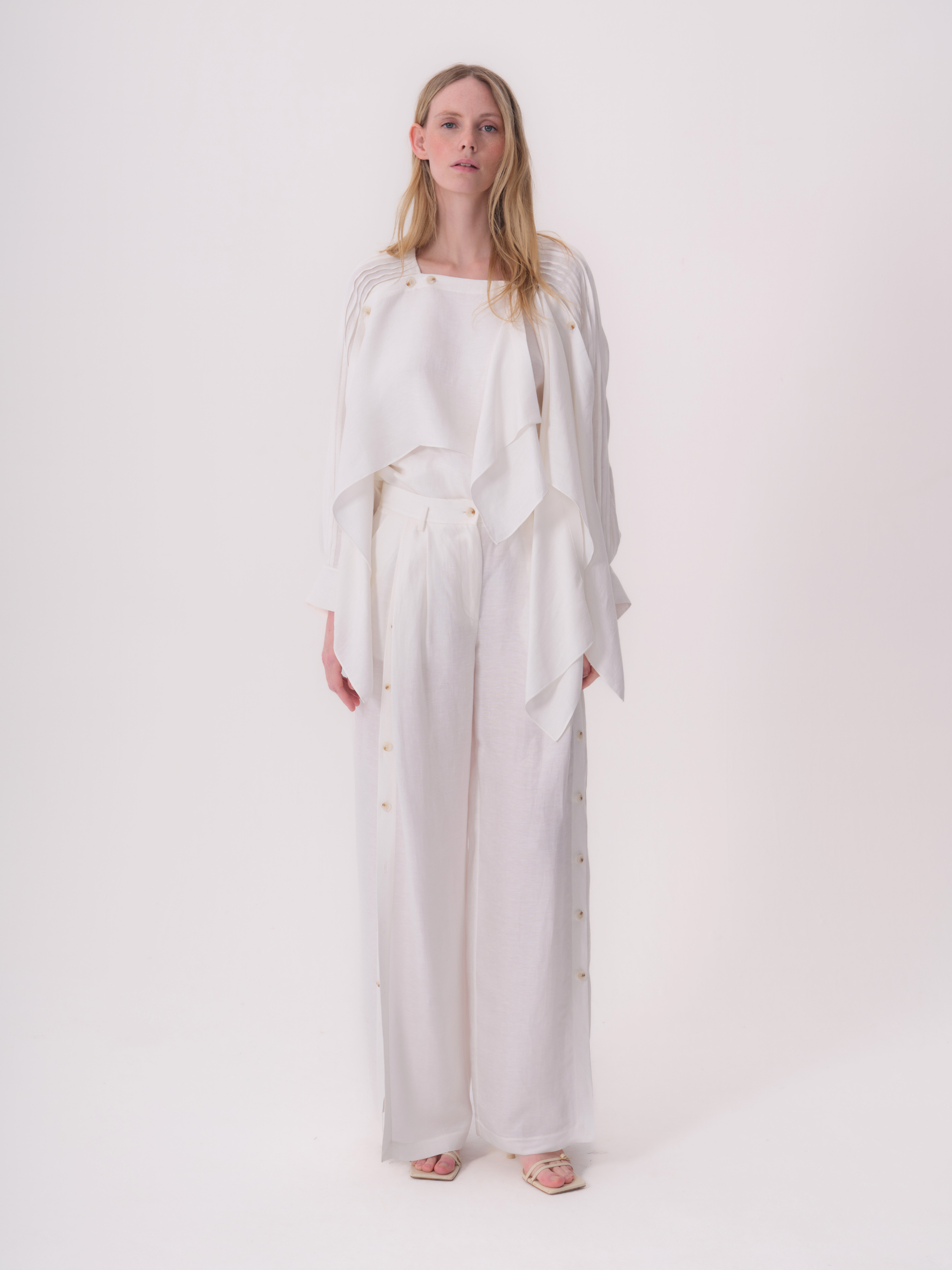 White wide-leg trousers with a high waist and a row of light brown buttons down both outer seams.