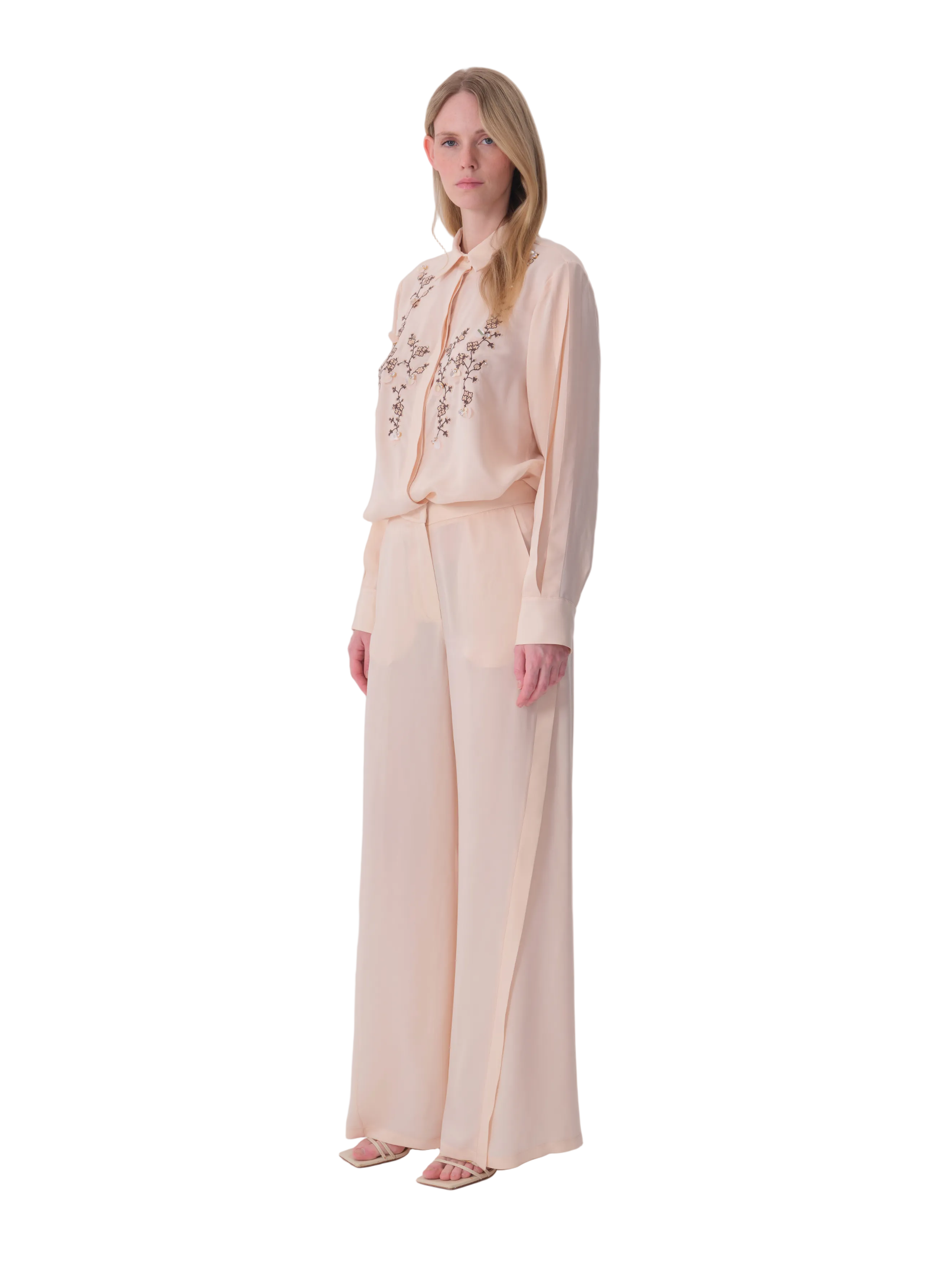 Beige wide-leg trousers made of a light, flowing fabric, with a high waist and a vertical seam down each leg.