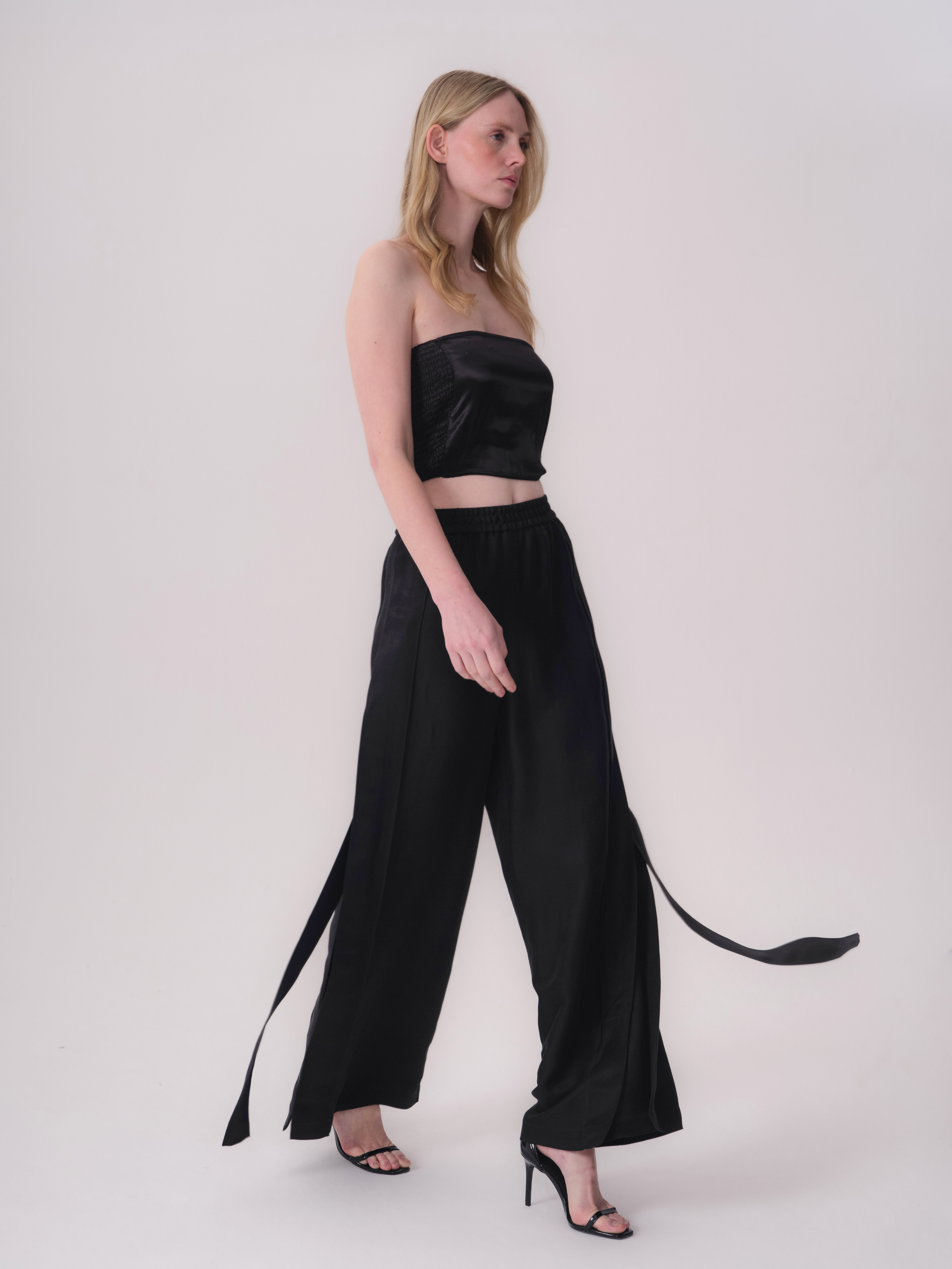 Black wide-leg trousers with an elasticated waistband and long, flowing fabric ties on the outer seams.