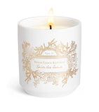 White ceramic scented candle with gold-toned foliage and text design, featuring a single lit wick.