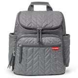 Grey quilted backpack with chevron stitching, multiple zippered pockets, side slip pockets, and a top carry handle.