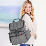 Grey quilted backpack with zigzag pattern, multiple front zippered pockets, side pocket, top handle, and shoulder strap.