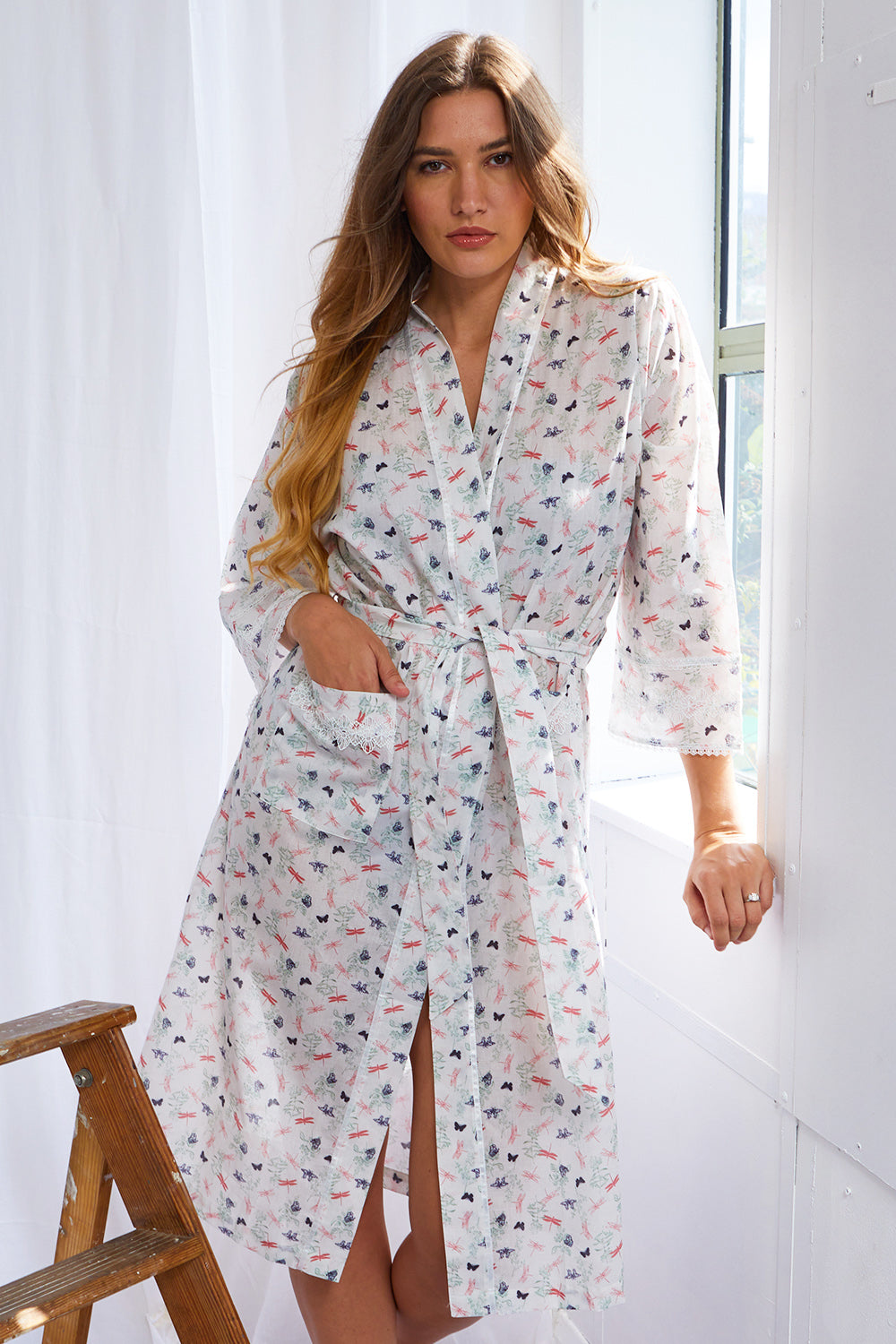 White voile kimono wrapover with butterfly flora print. Self-tie belt, V-neck, 3/4 sleeves, and lace-trimmed pockets.