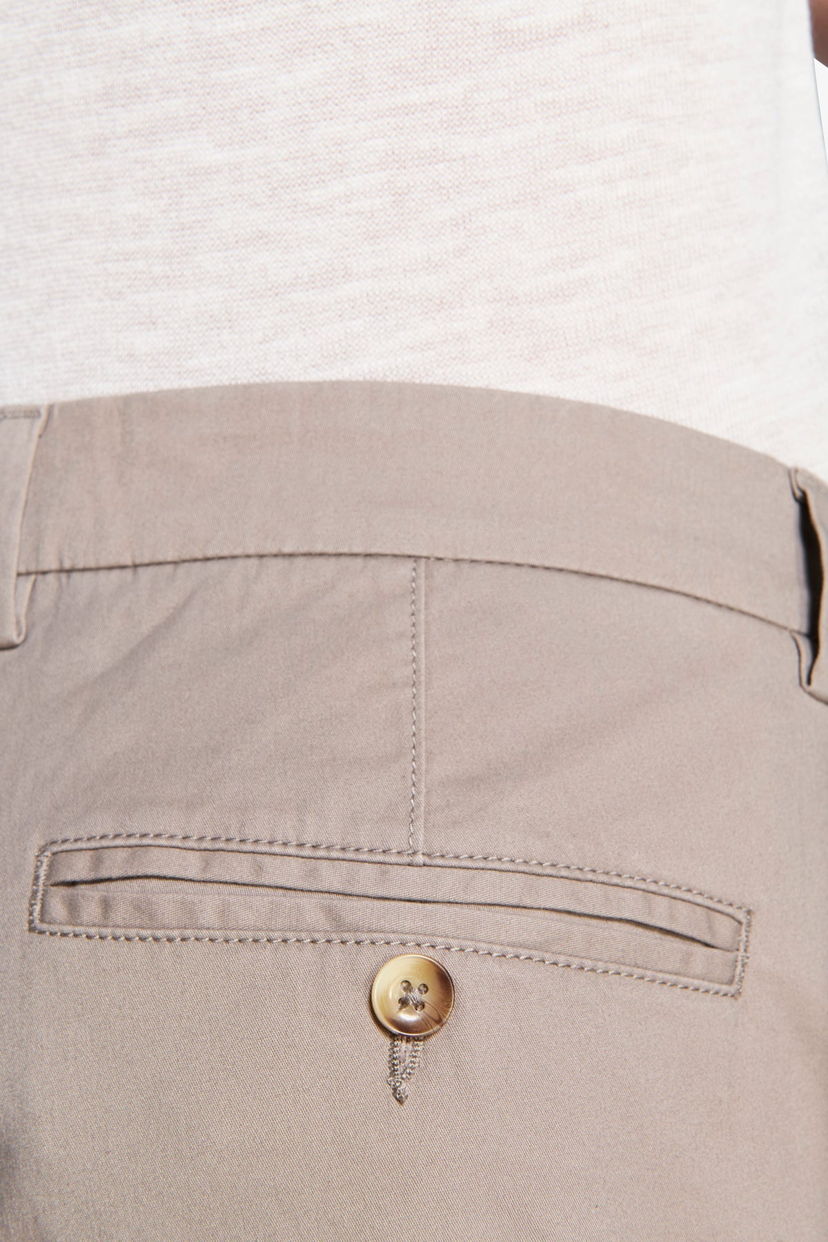 Taupe trousers with a flat waistband and a single welt back pocket featuring a light brown button below the opening.