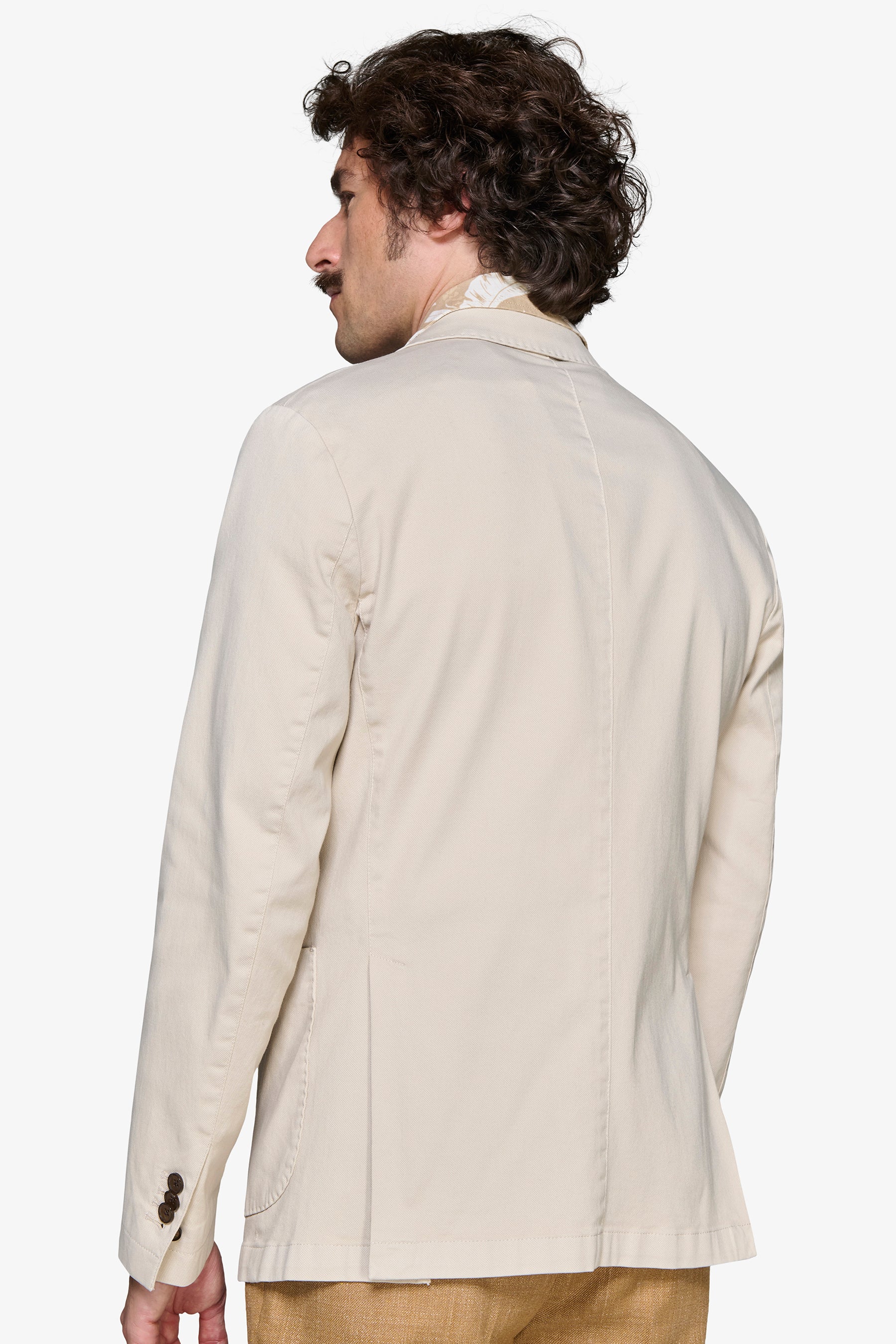 Light beige blazer with a single back vent, center back seam, and two dark brown cuff buttons on the right sleeve.